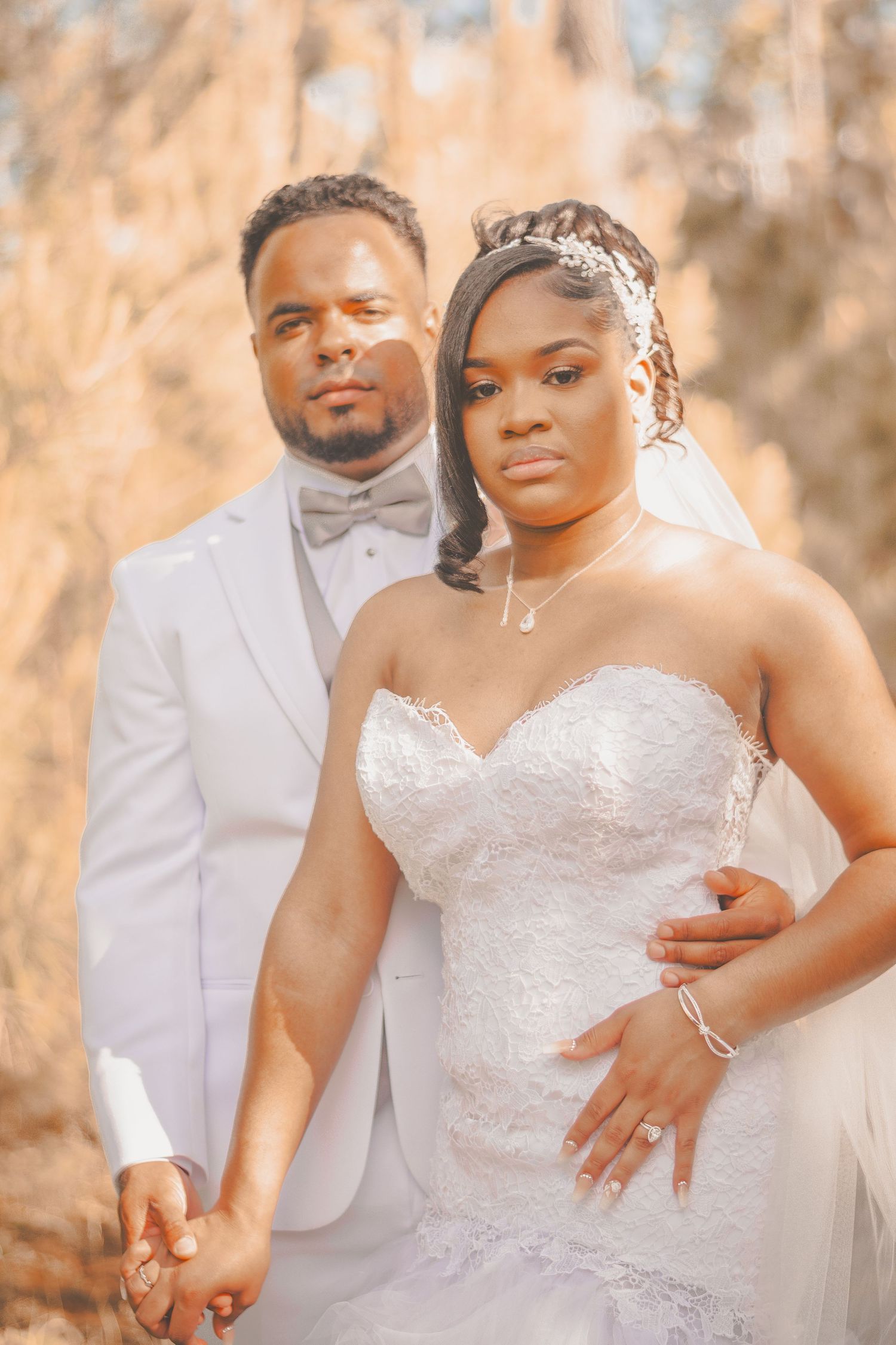 A wedding portrait featuring a couple in elegant white attire against a warm autumn backdrop.