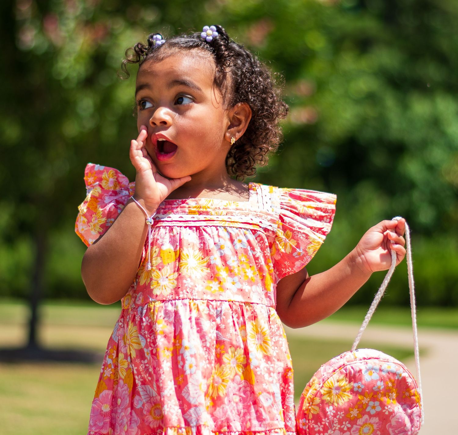 Young child in floral dress showing surprised expression while holding matching purse.