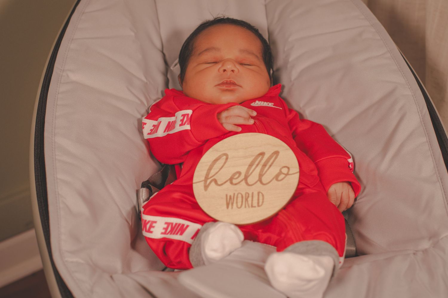 Sleeping newborn in red outfit with 'hello world' sign.