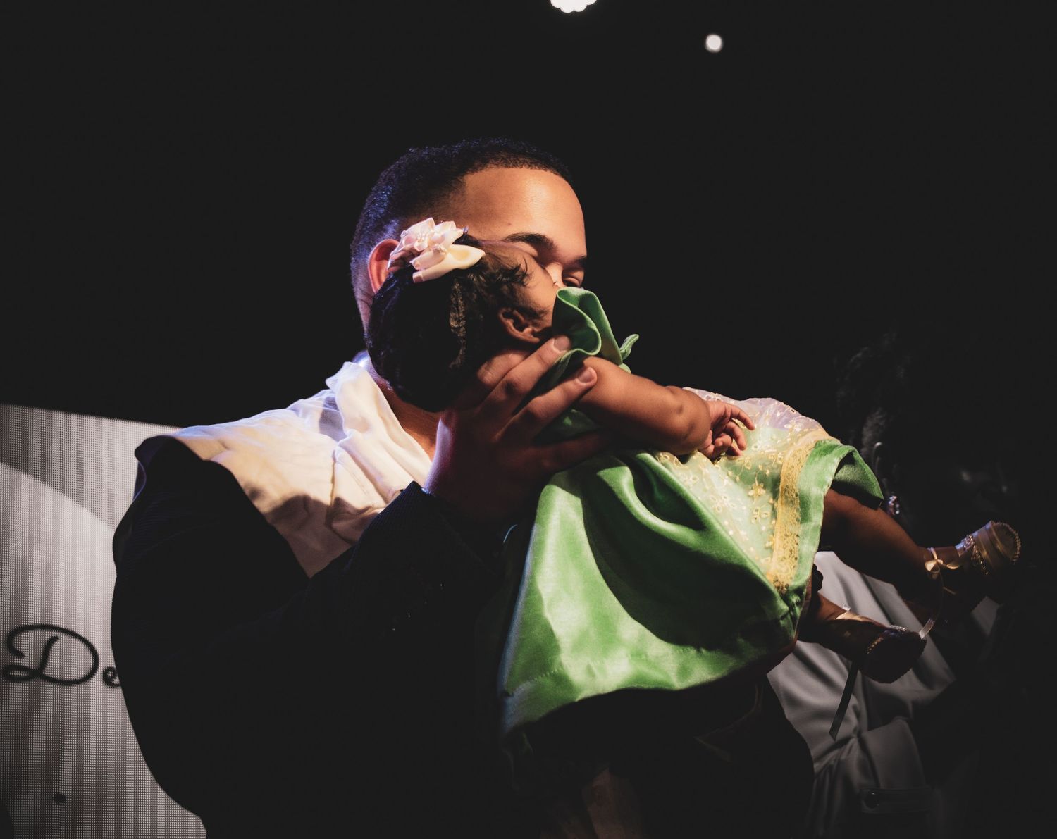 Concert performer holding green item while sitting on stage in dark lighting.