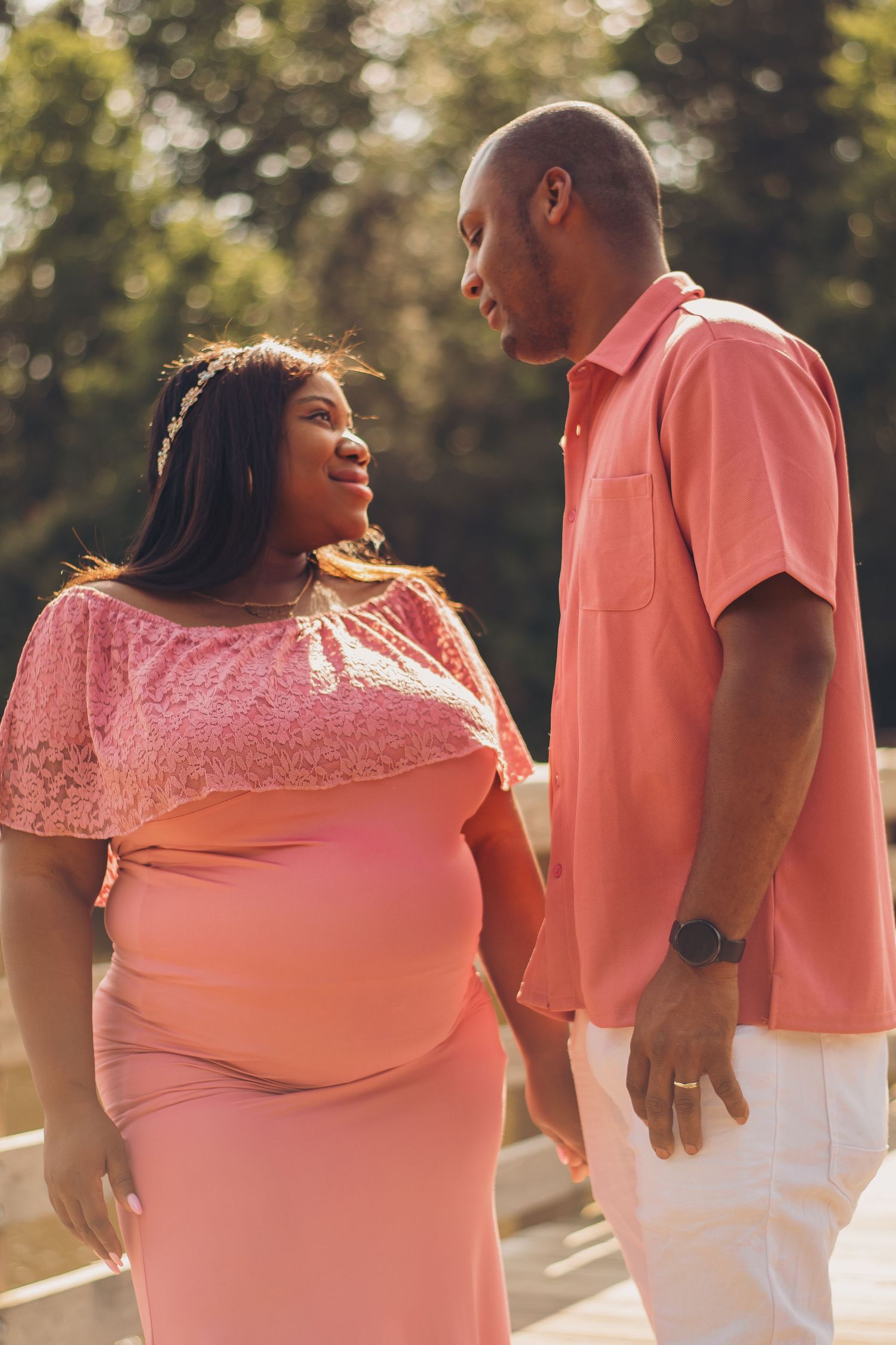 Couple in matching coral outfits sharing intimate moment outdoors during maternity photoshoot.
