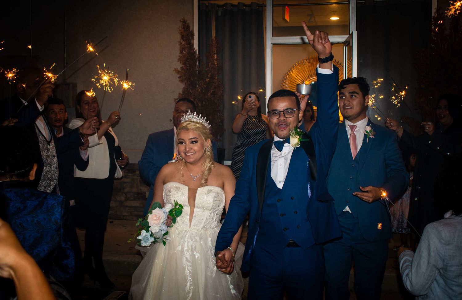 Wedding couple walking through sparkler exit with guests lining path at night.