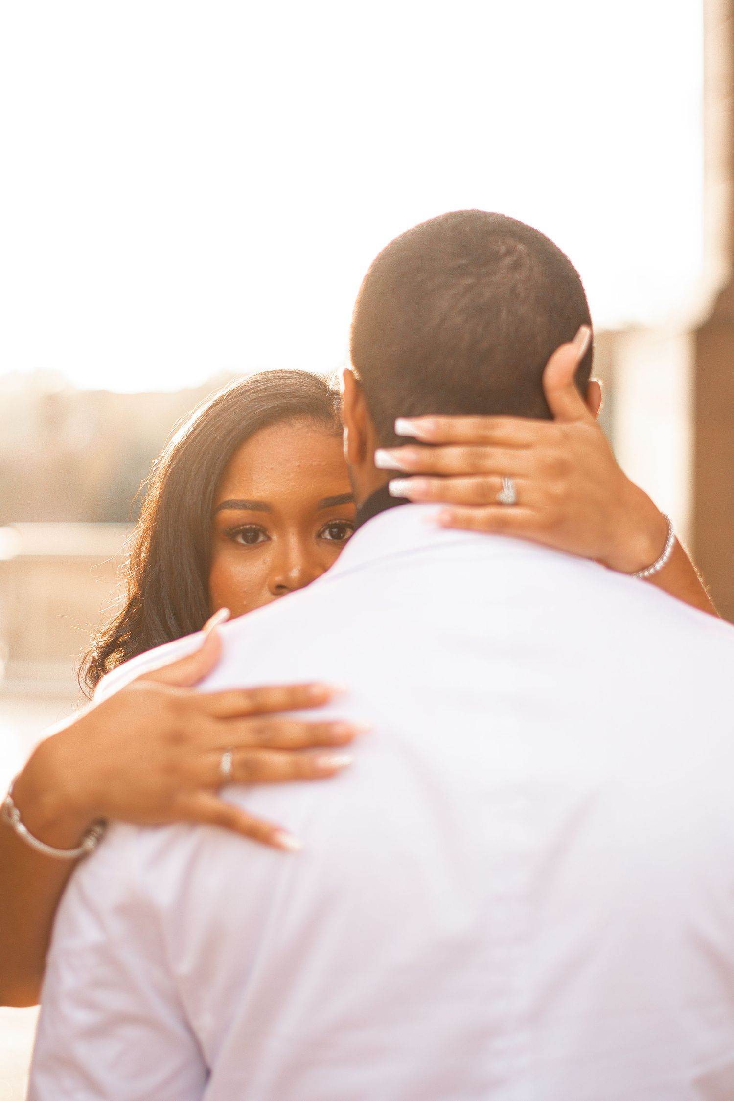 Warm sunset photo of couple embracing, with engagement ring visible on woman's hand.