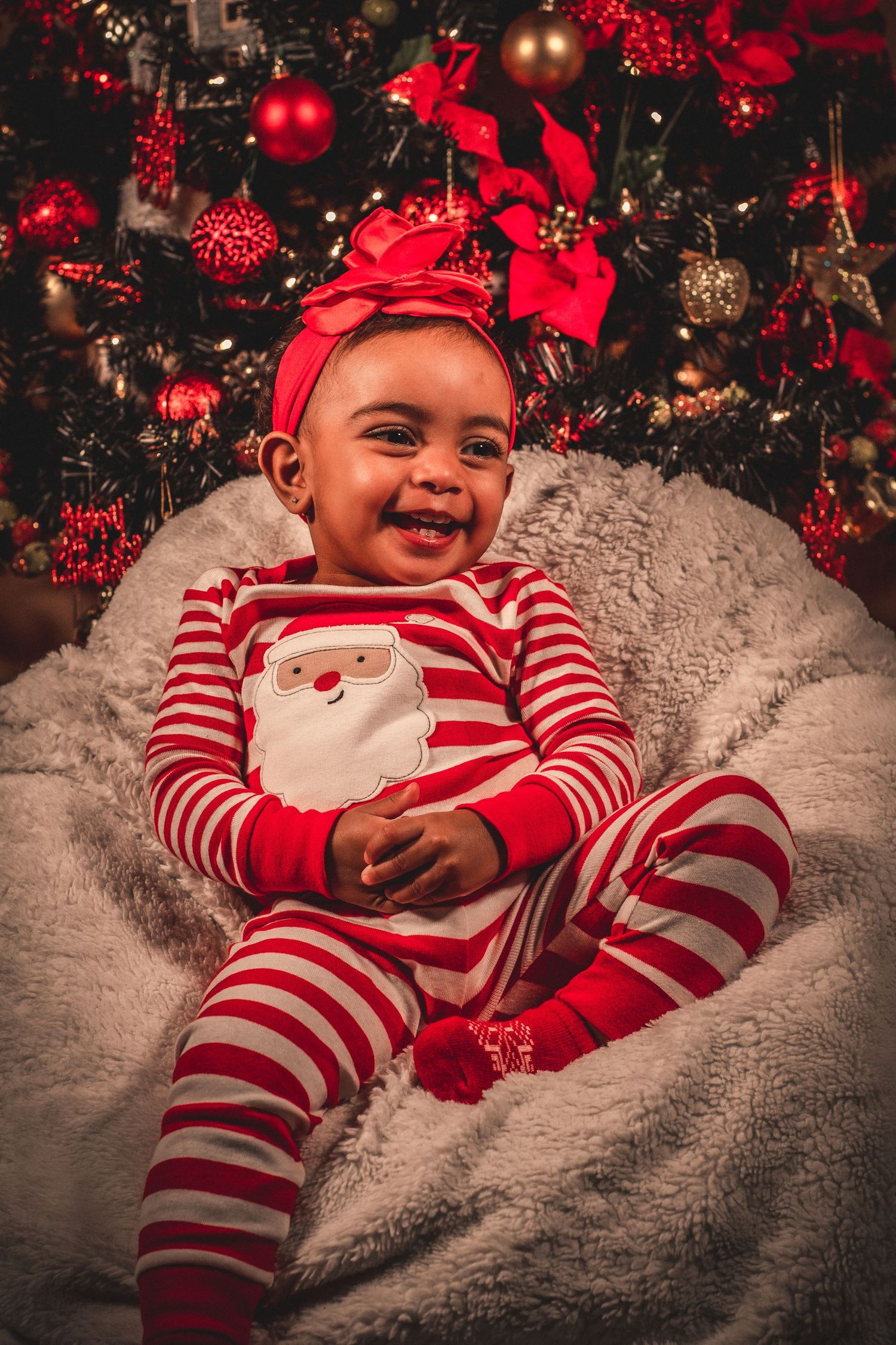 Holiday portrait in front of Christmas tree with red and white striped Santa pajamas.