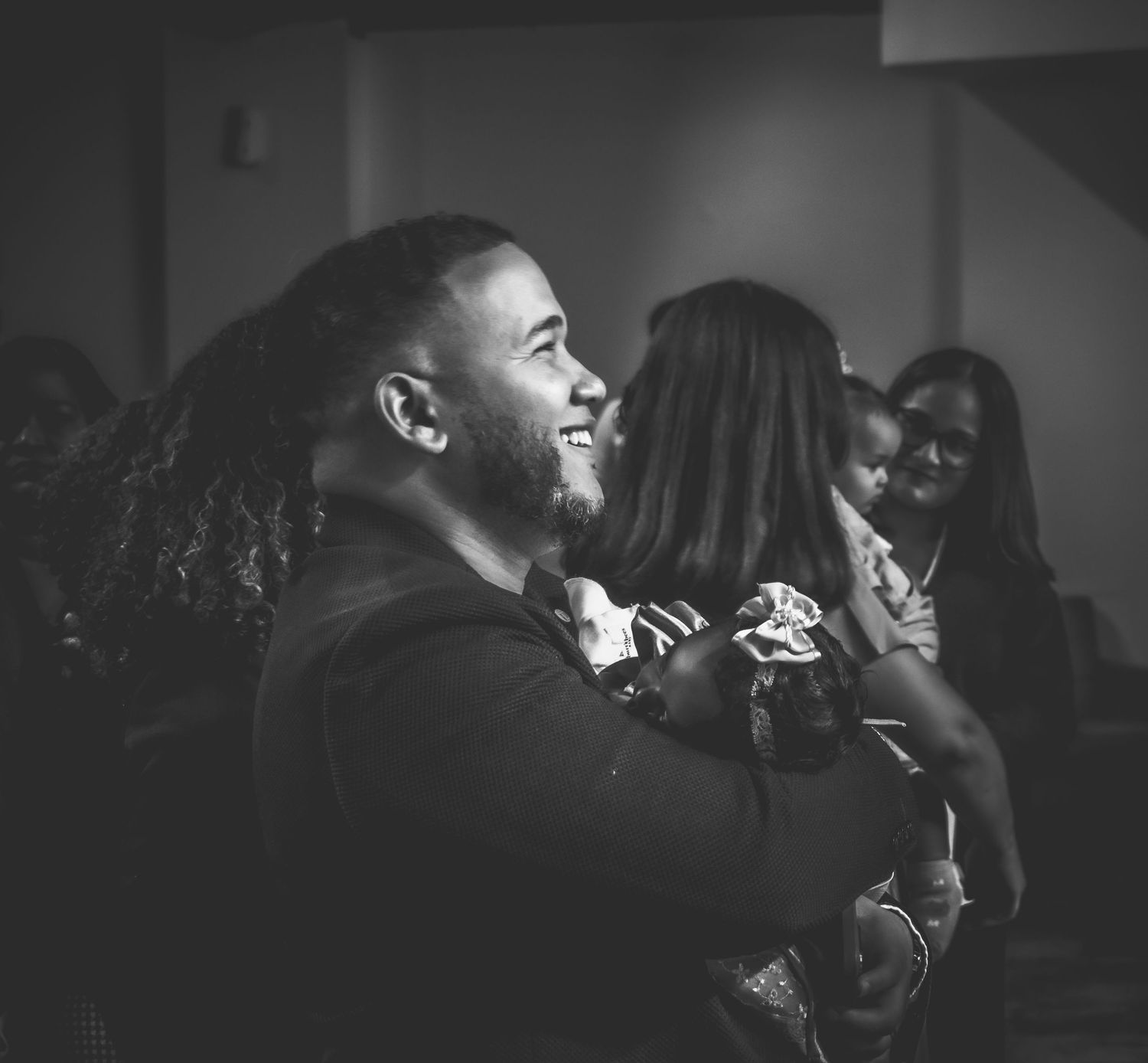 Black and white photo of a smiling man with long hair at a formal event surrounded by guests.