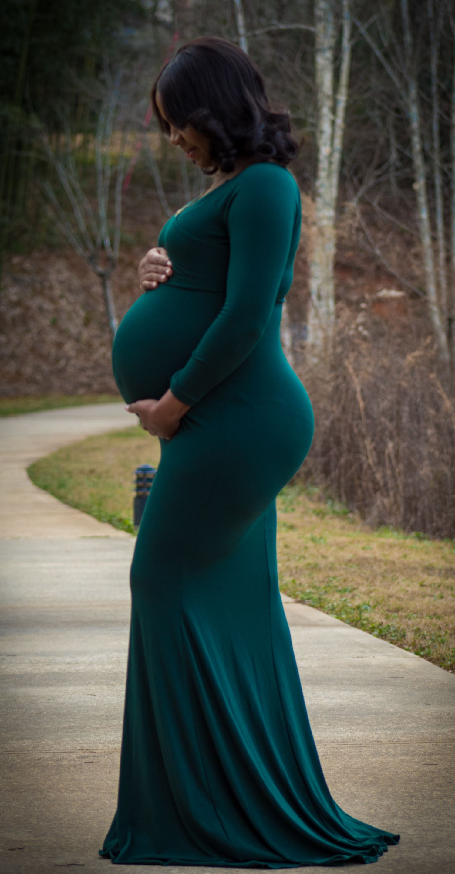 Elegant maternity photo of woman in flowing teal gown on curved pathway.