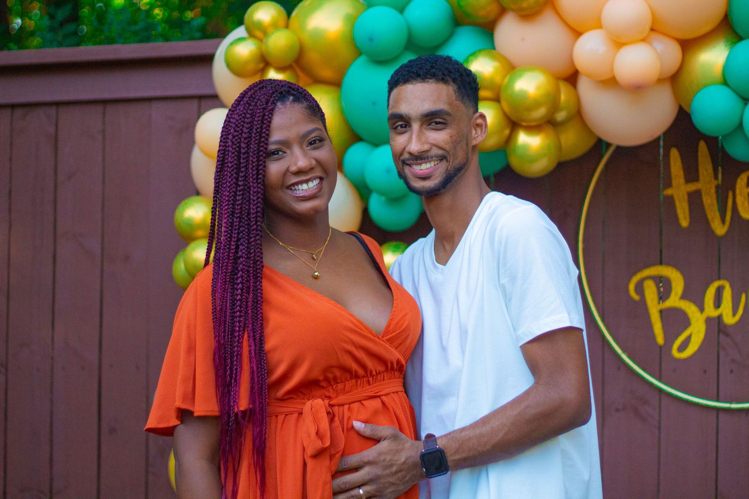 A couple poses in front of colorful balloon arch during outdoor celebration.