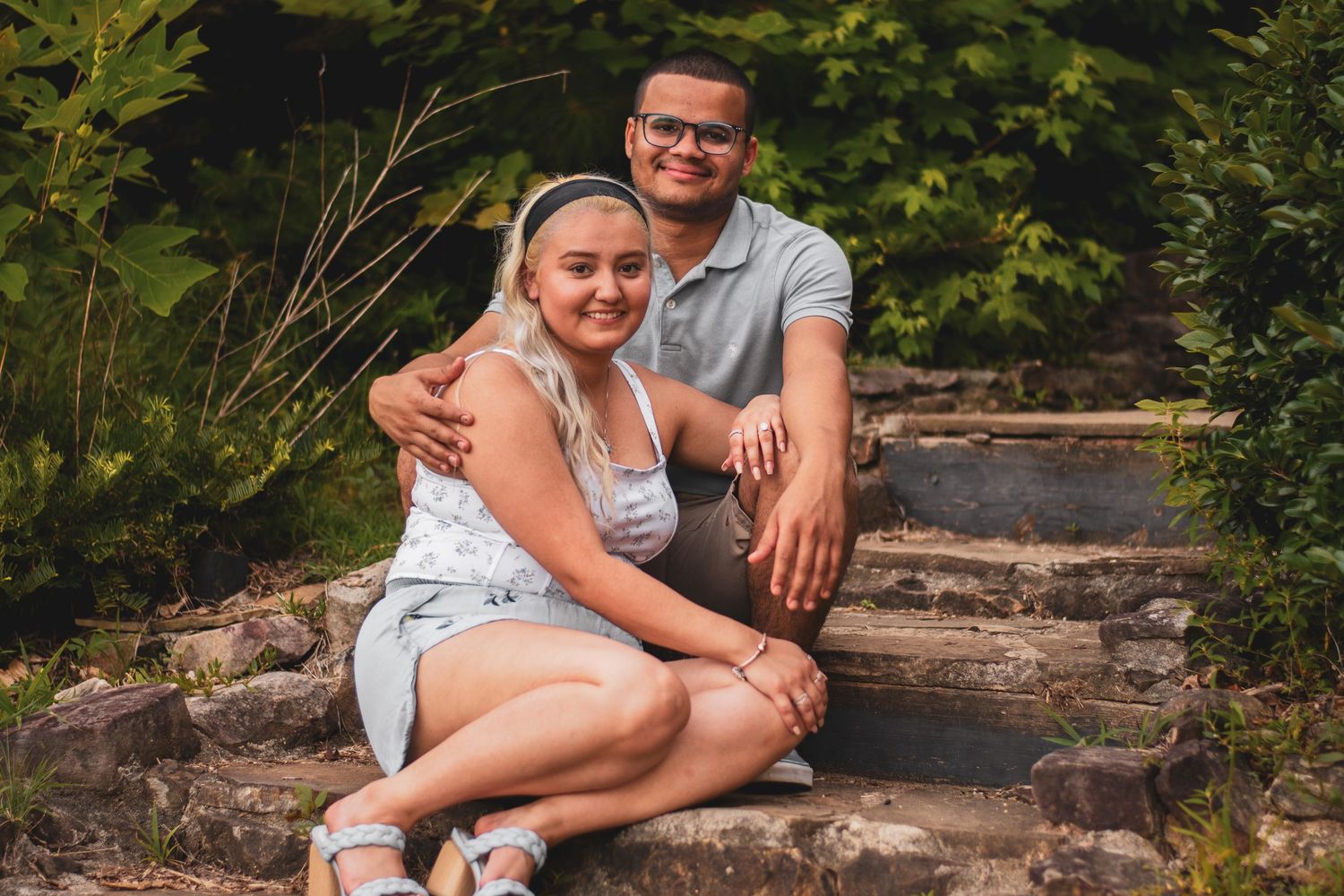Couple sitting together on stone steps in lush garden setting.