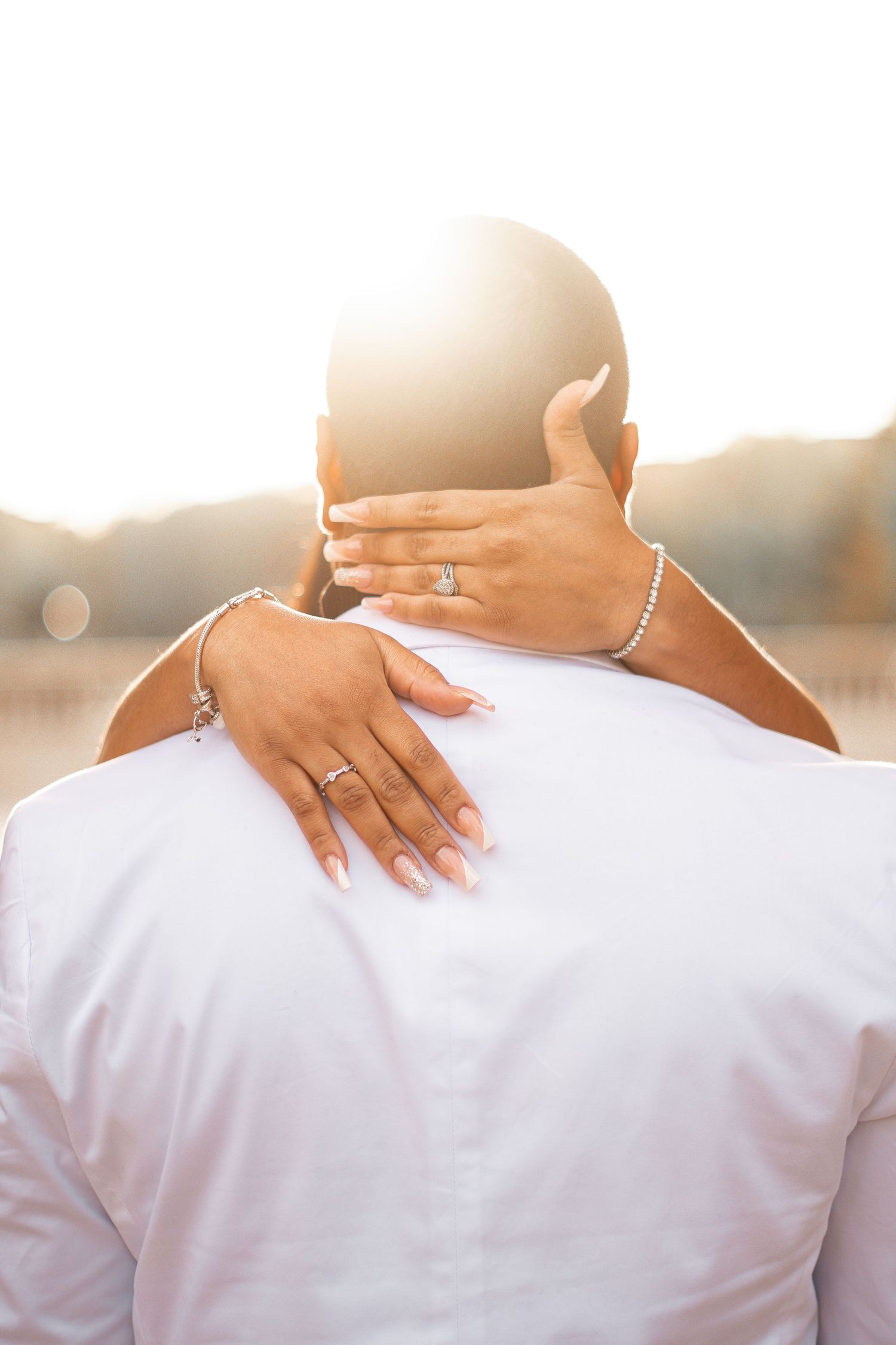 Romantic golden hour portrait showing hands with jewelry embracing from behind.
