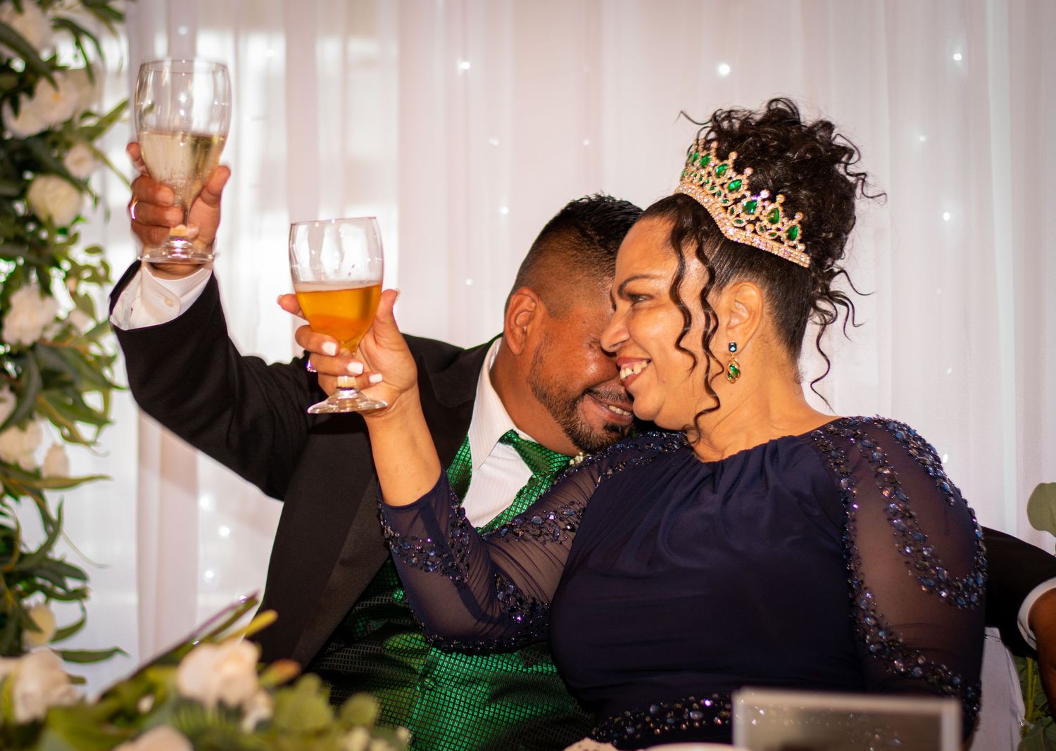 A couple toasts with glasses during their wedding reception while dressed in formal attire.