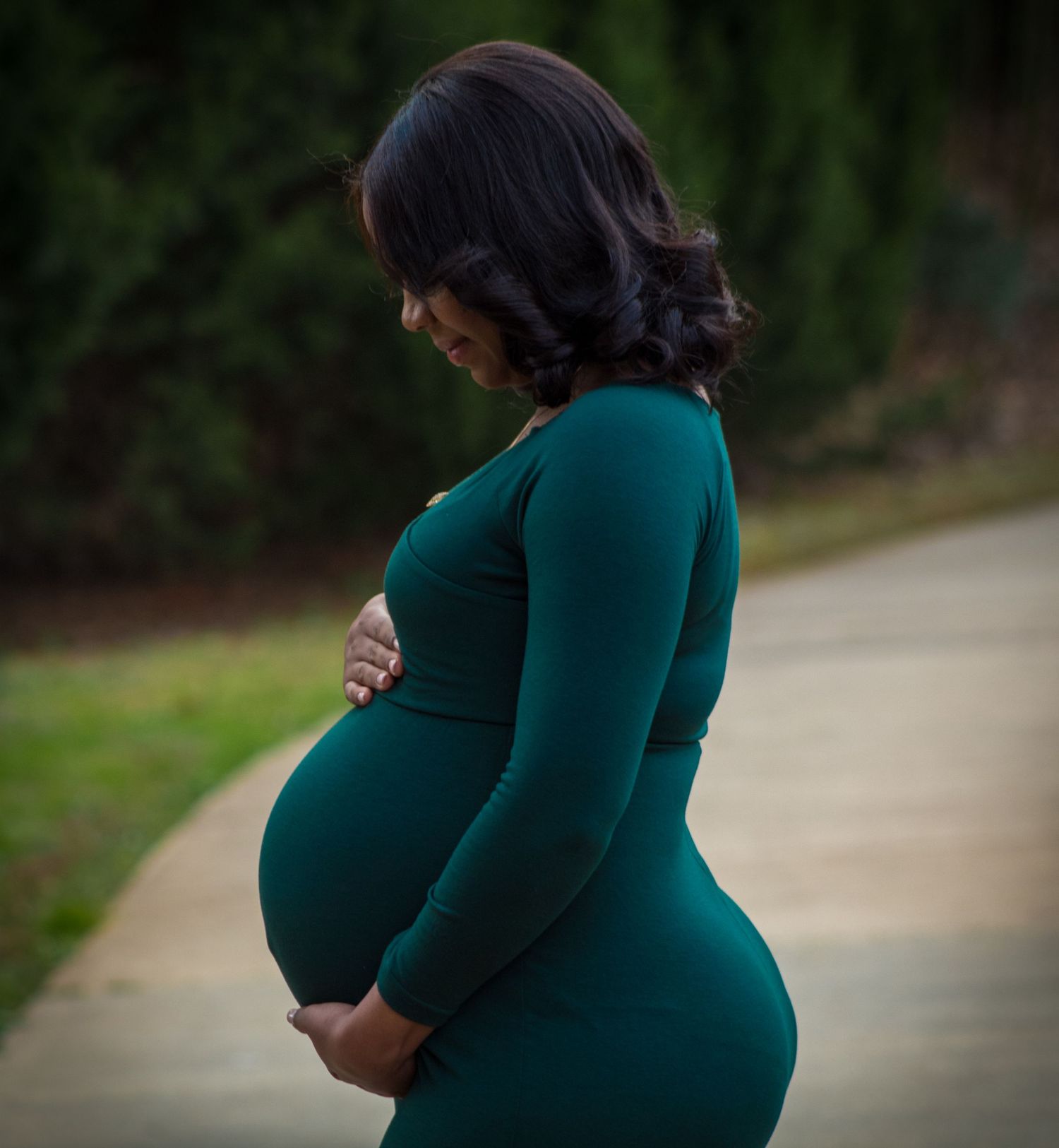 Silhouette of pregnant woman in teal dress standing on outdoor path.