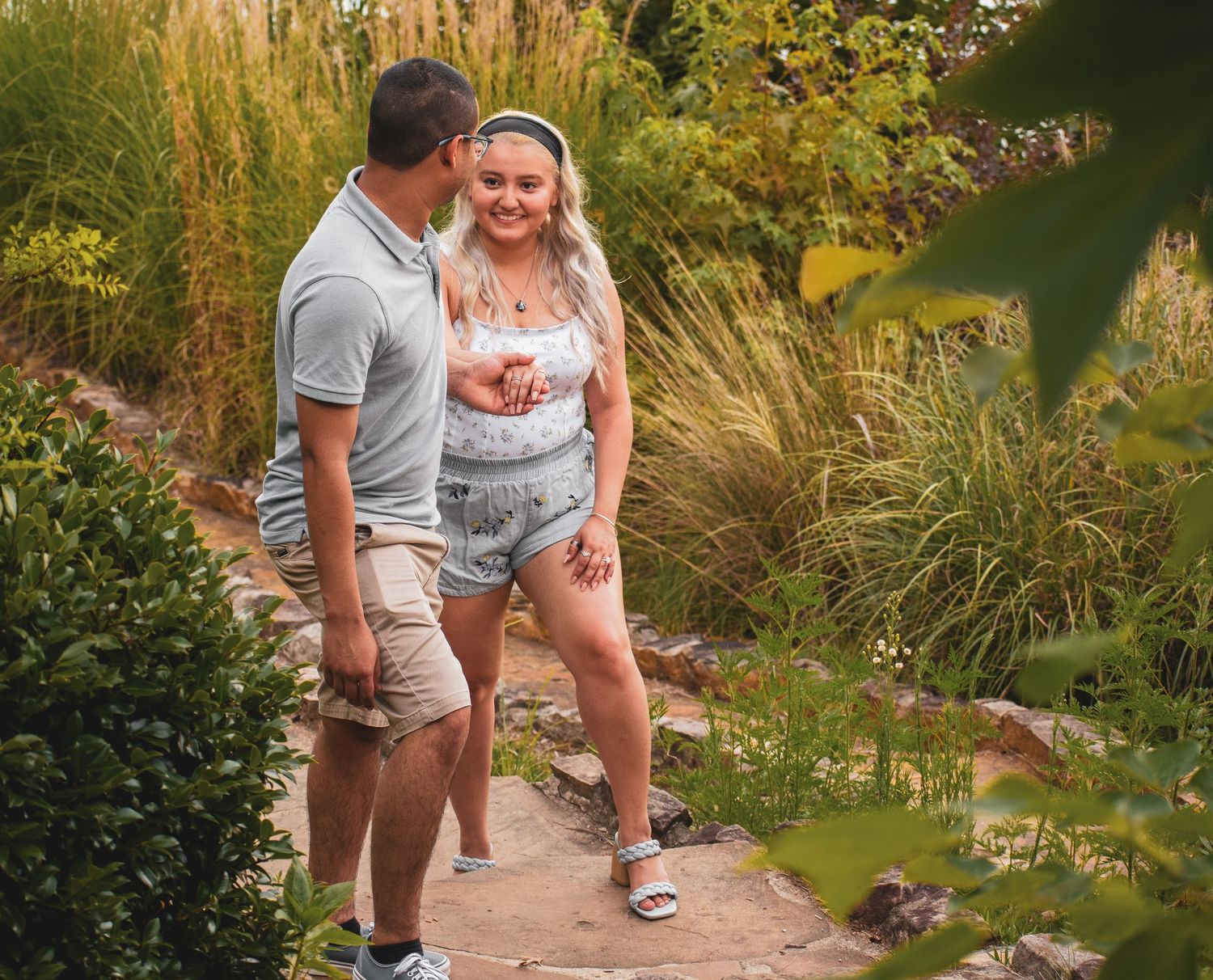 Couple sharing a laugh while walking on garden path surrounded by tall grasses.