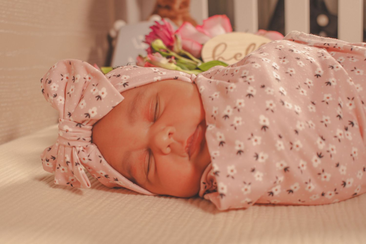 Sleeping newborn baby wearing pink floral outfit and matching headband.