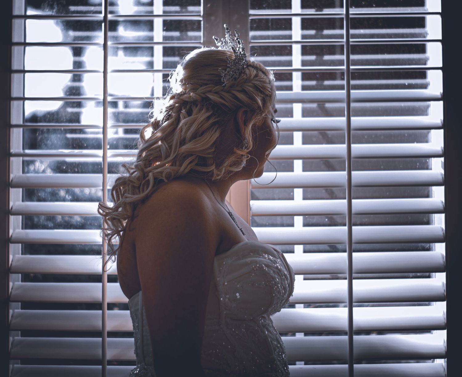Silhouette of bride in wedding dress against window with venetian blinds.