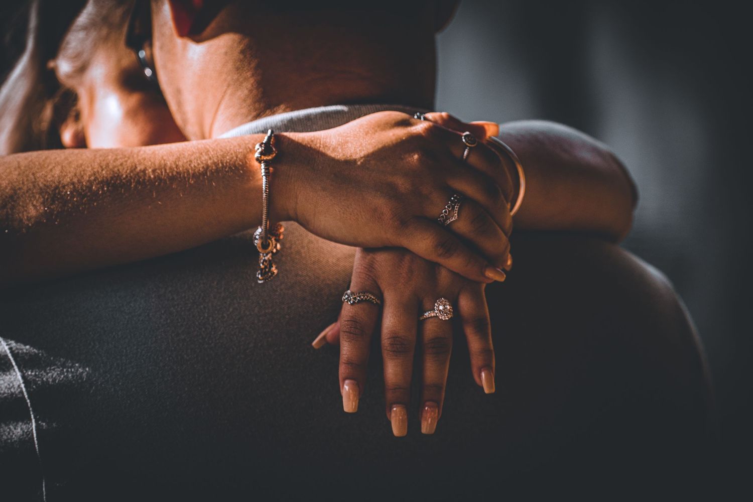 Close-up of hands with engagement ring and bracelet in dramatic lighting.