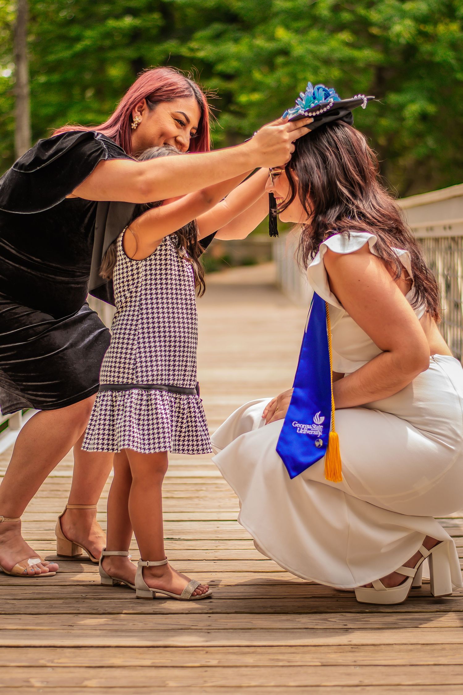 Graduation celebration moment between three people on wooden bridge.