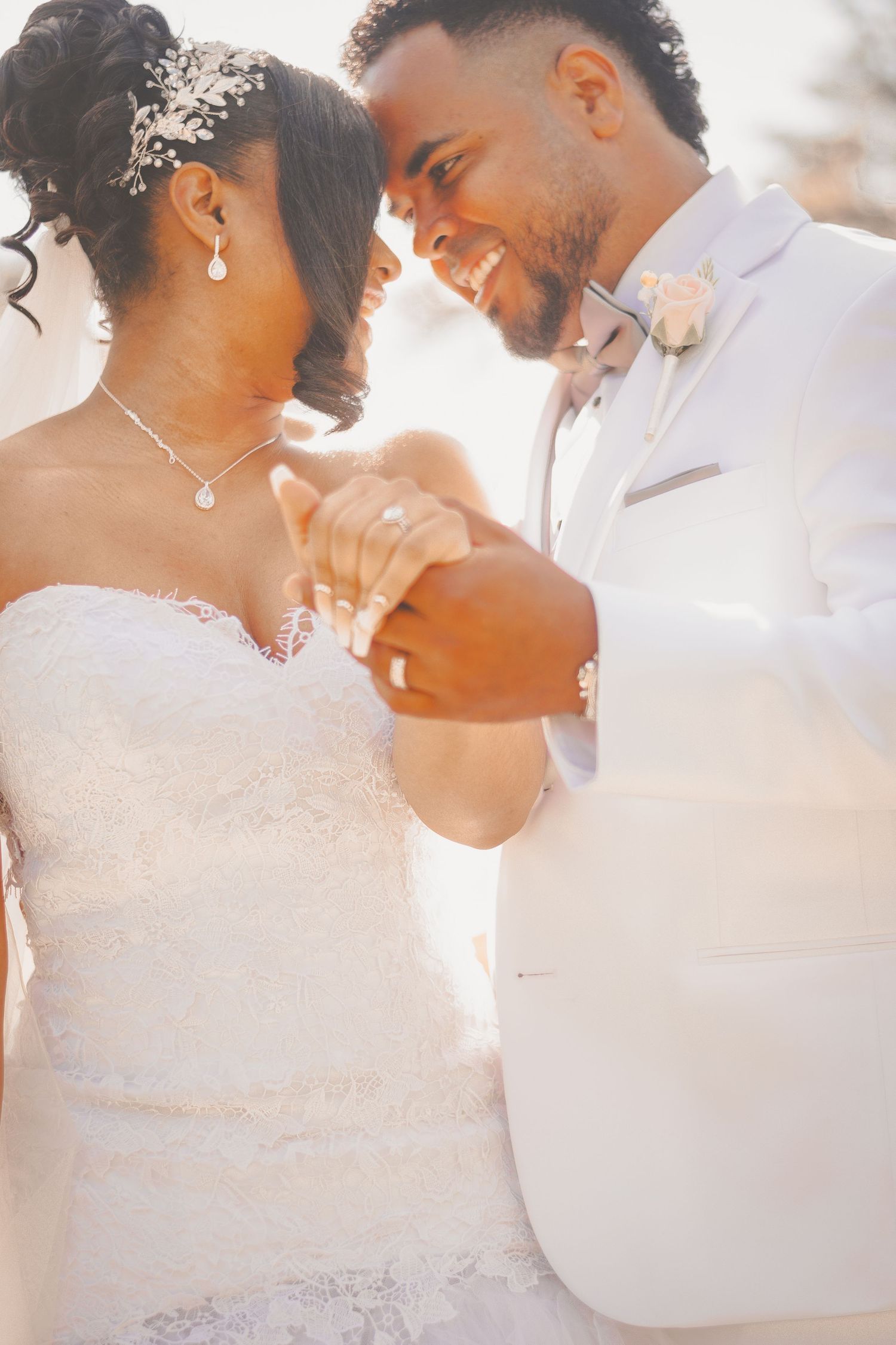 A romantic moment between newlyweds showing their wedding rings while dressed in white formal attire.