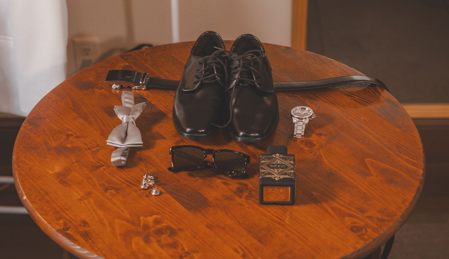 A pair of black dress shoes and cuff links arranged on a rustic wooden round table.