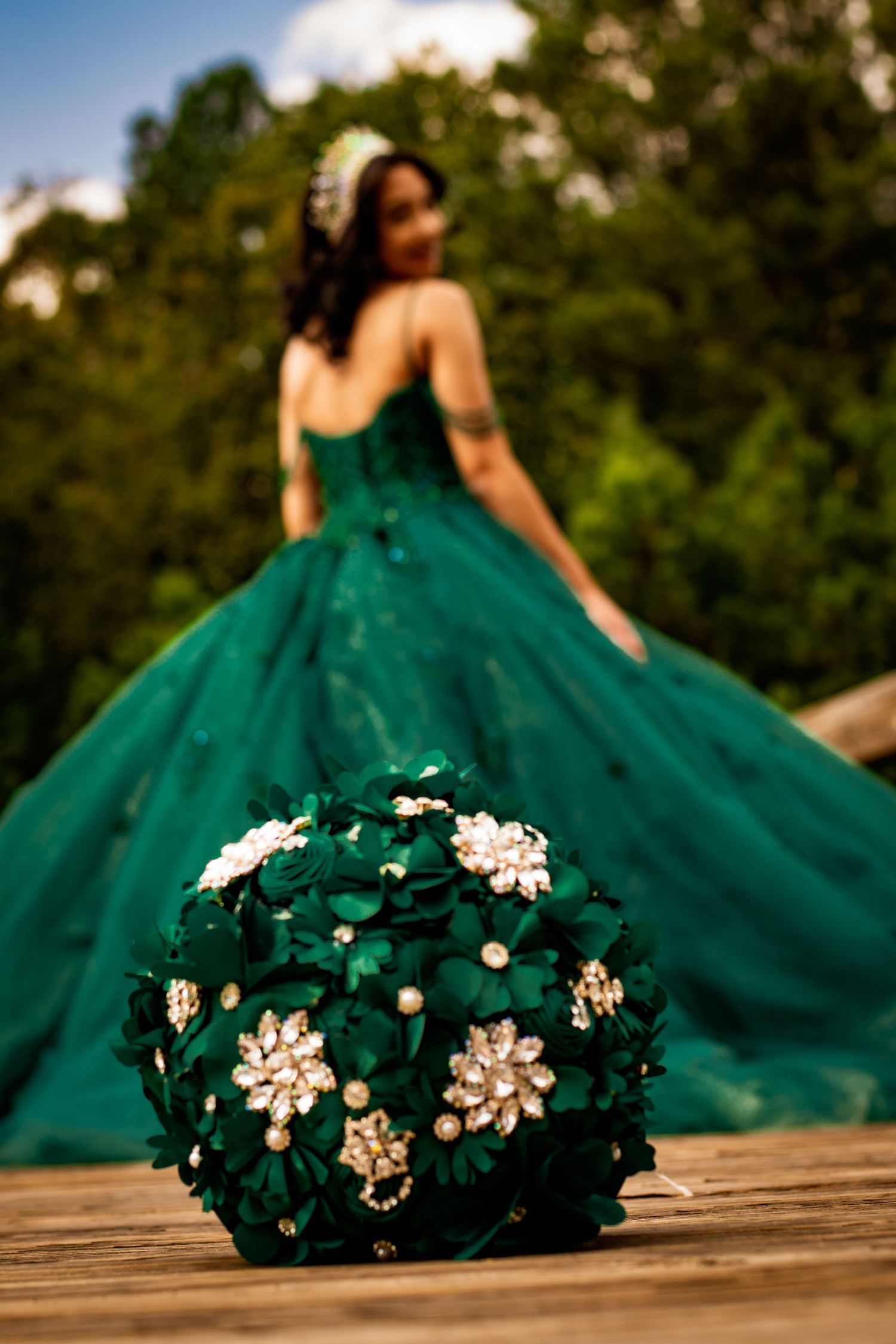 A creative shot focusing on a floral bouquet with a green ball gown silhouette in the background.
