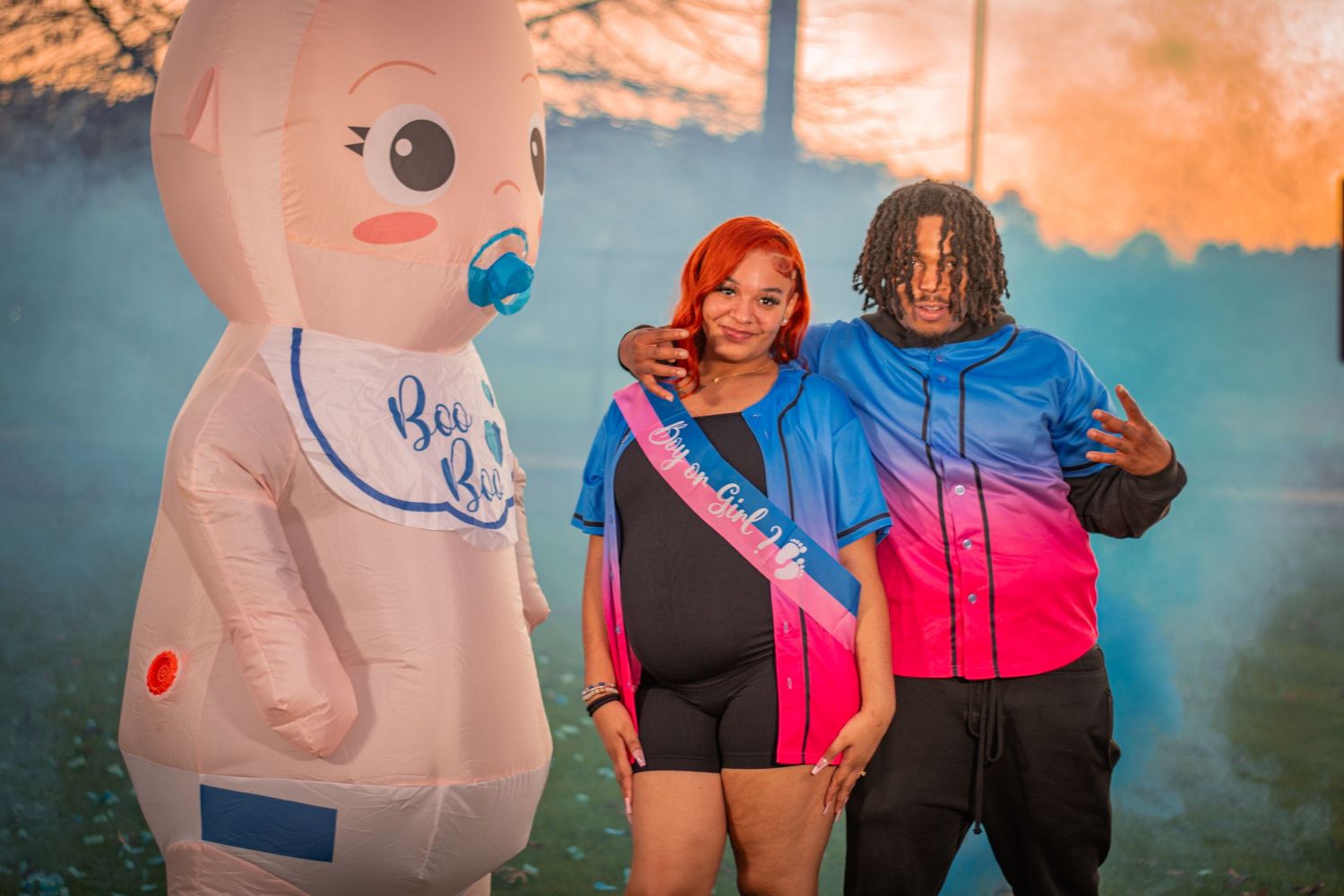 A couple poses with an inflatable baby decoration during a gender reveal photoshoot.