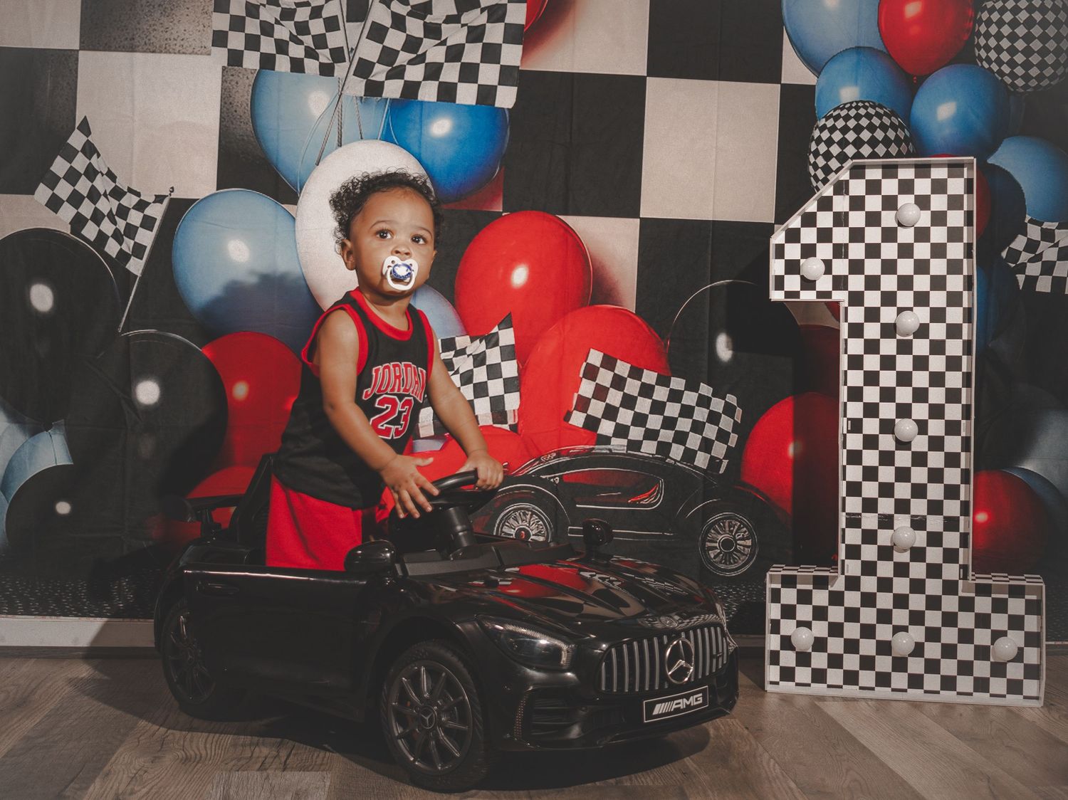 Kids toy car racing party setup with checkered flags, red and blue balloons against black and white backdrop.