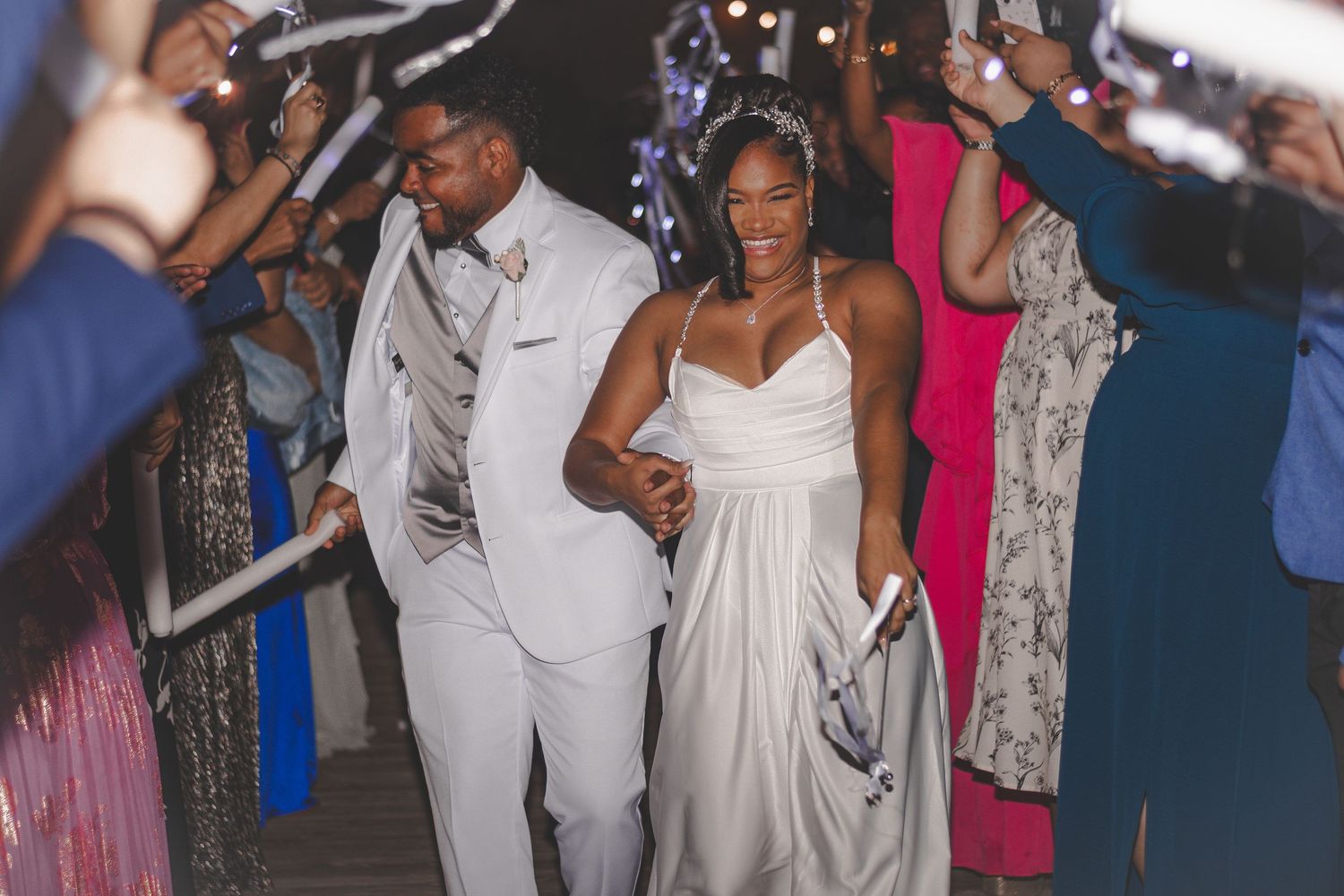 Wedding reception guests in formal attire celebrate in a lively tunnel of sparklers during a nighttime exit celebration.