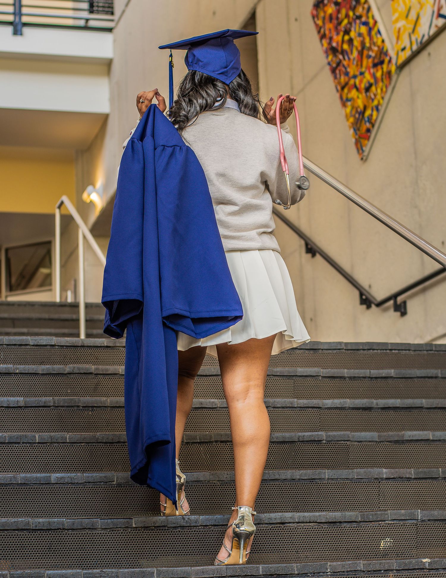A graduate ascends stairs while carrying blue graduation regalia.