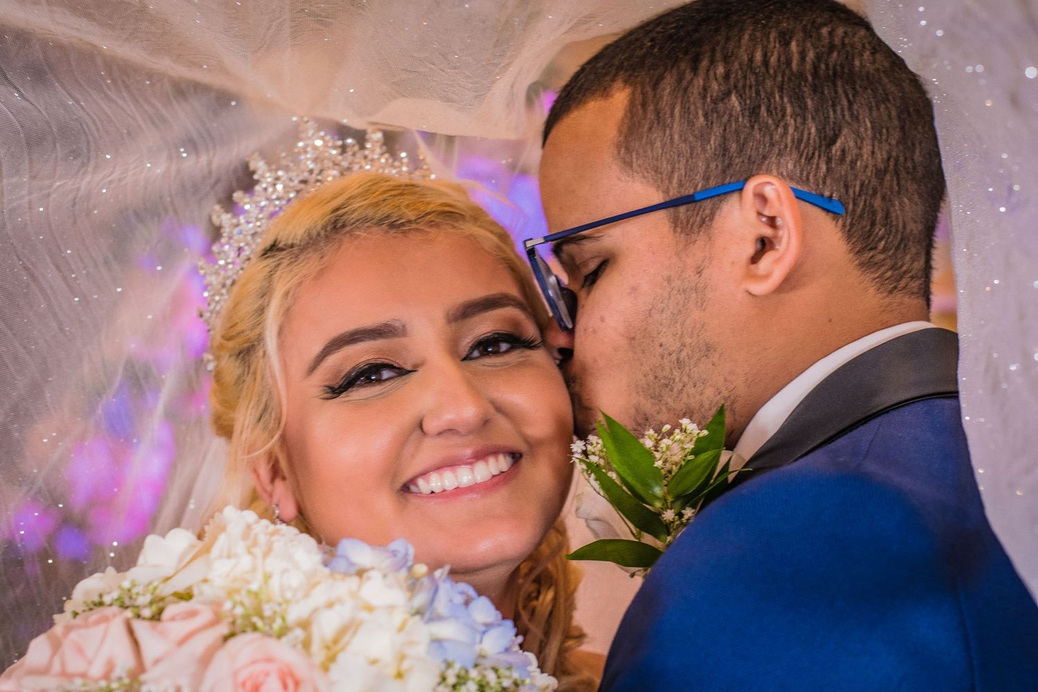 Intimate wedding portrait of a couple sharing a tender moment amidst purple lighting and floral decorations.