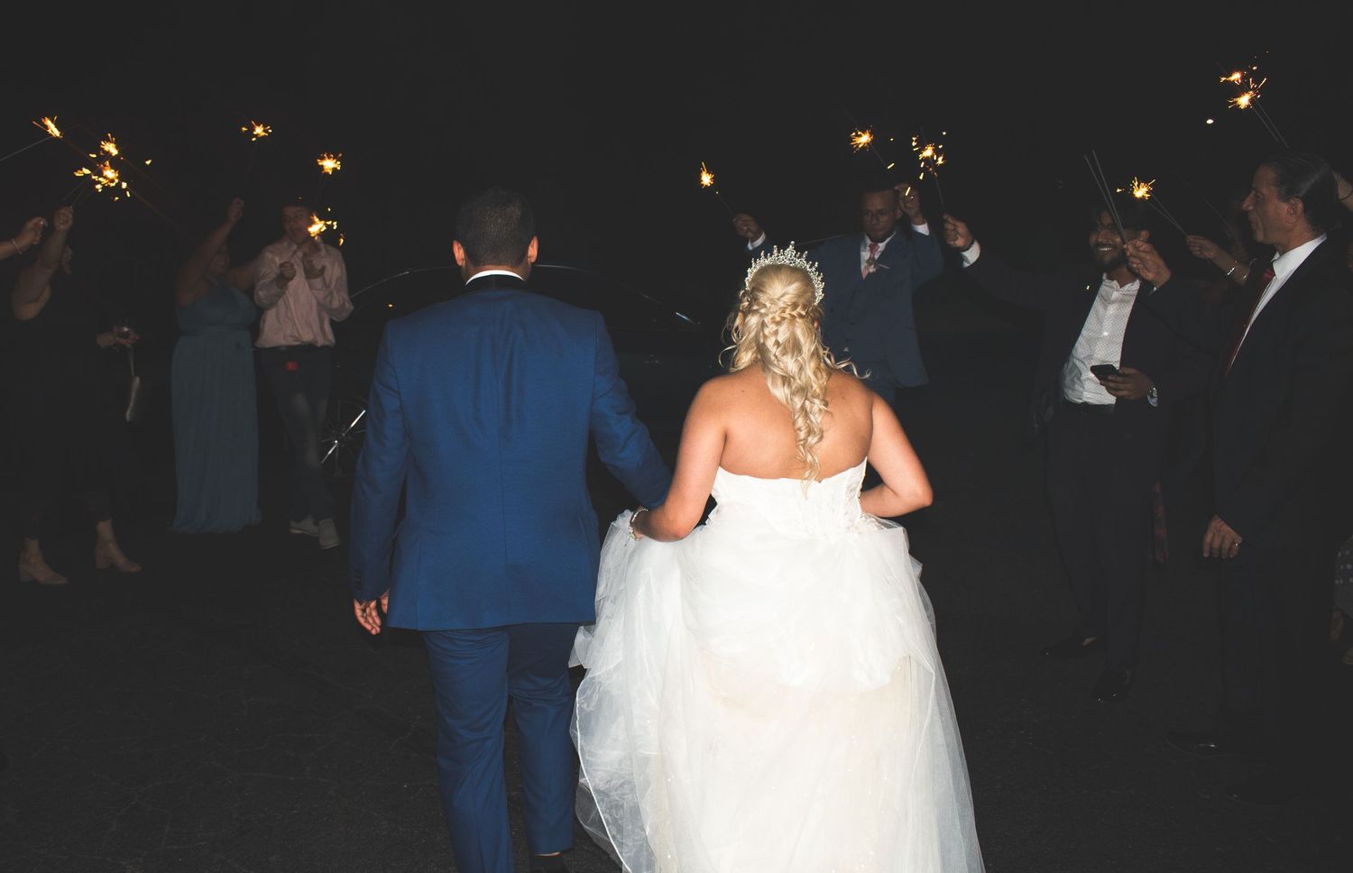Newlyweds walk through sparklers during nighttime wedding reception exit.
