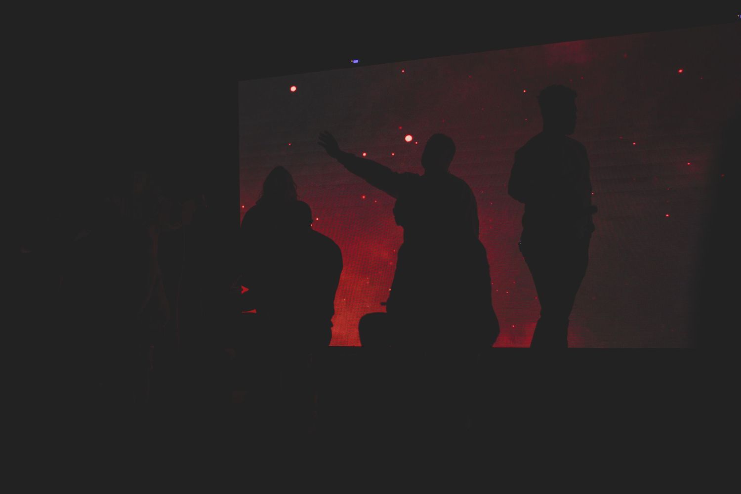 Silhouettes of people against a red backlit background creating dramatic shadows.