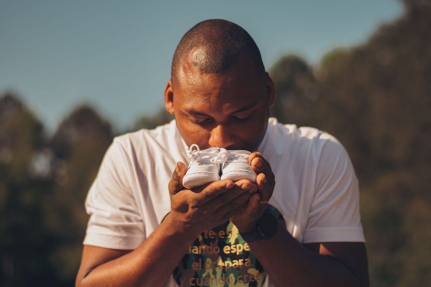 Person in white t-shirt tenderly holds and kisses a newborn baby.