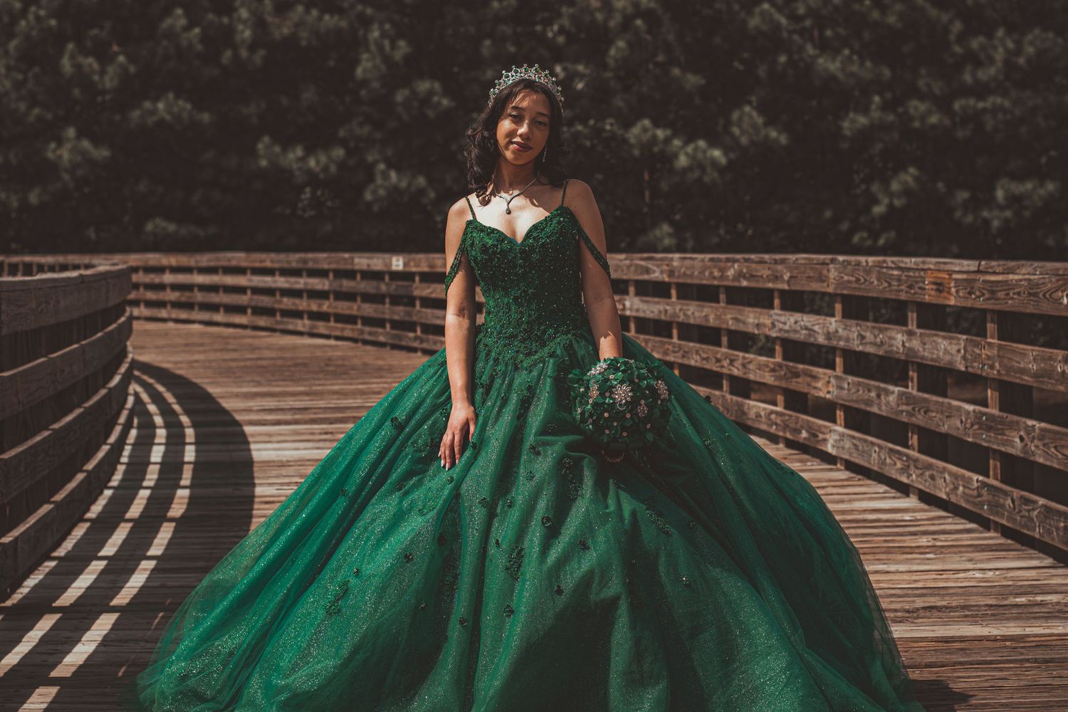 A full-length shot of an emerald green ball gown on a wooden bridge walkway.