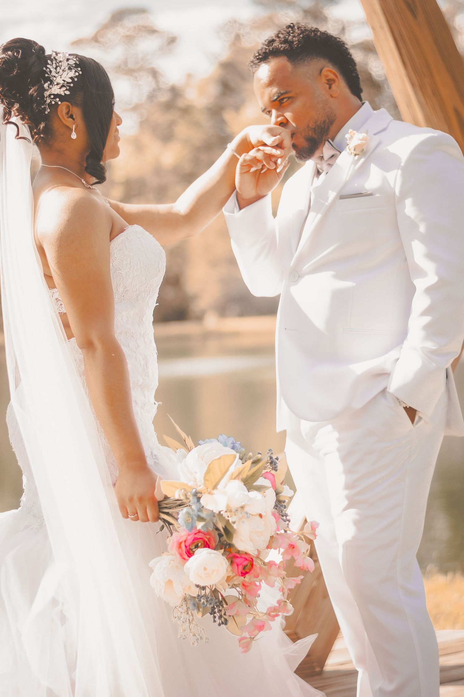 A touching wedding moment as the bride holds a pink and white bouquet while the groom kisses her hand.