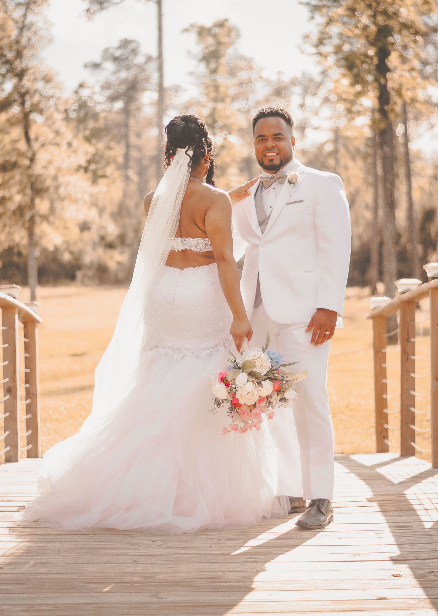 Sunlit wooden boardwalk wedding photos showing couple in white dress and suit against autumn background.