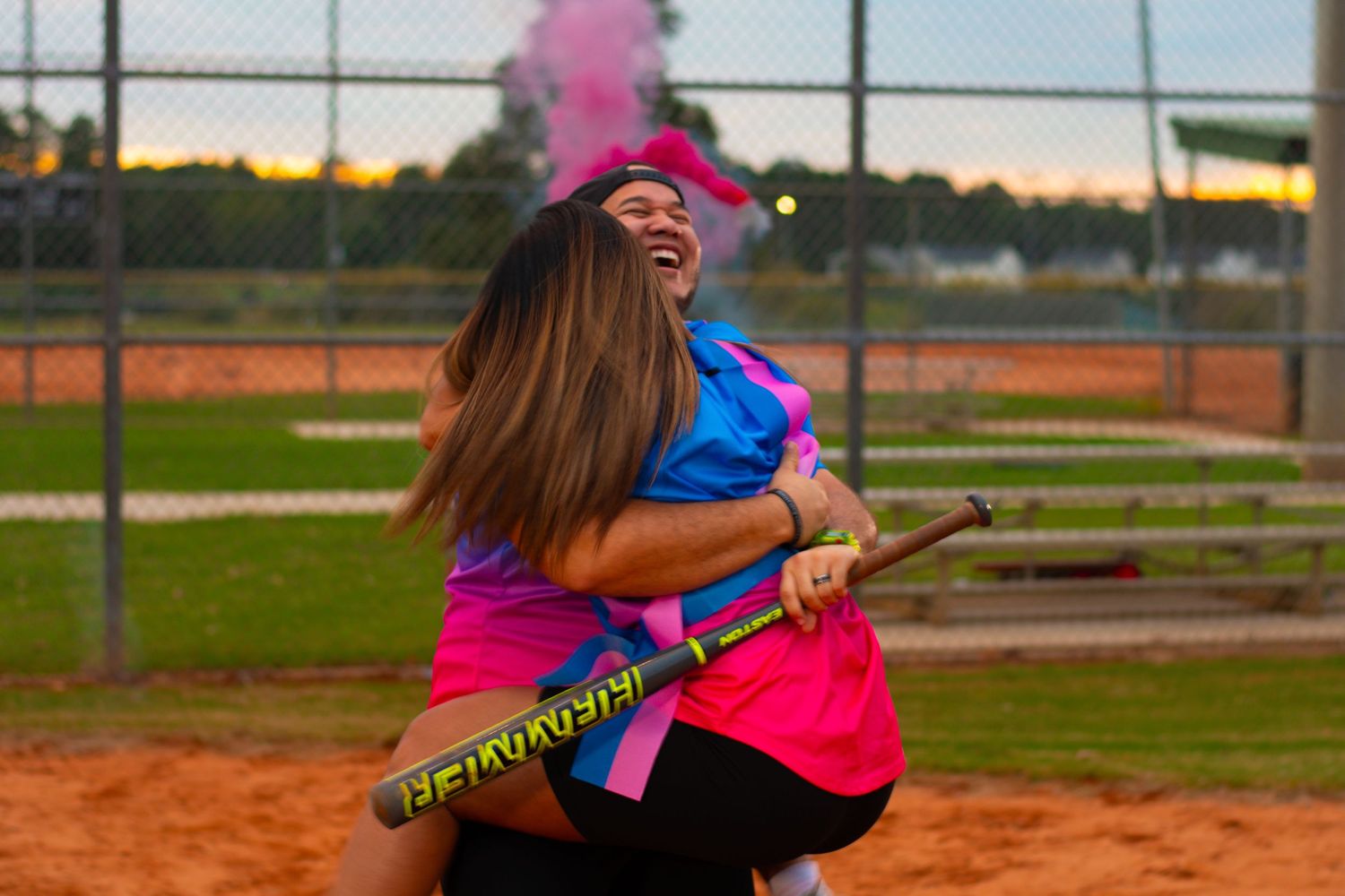A joyful moment captured on a baseball field with pink smoke and a baseball bat against a sunset sky.