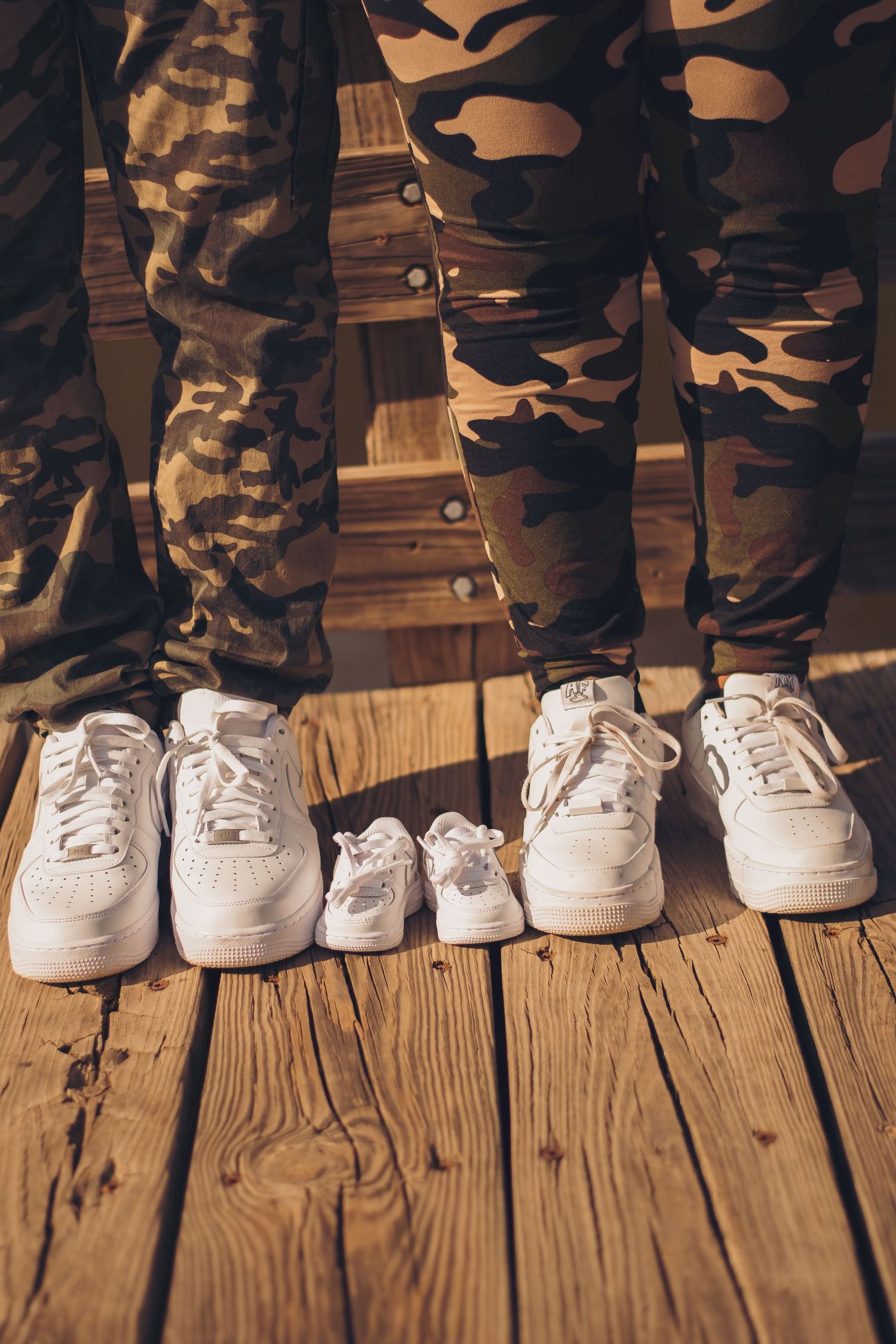 Row of white sneakers arranged in descending size on wooden deck with camouflage pants.