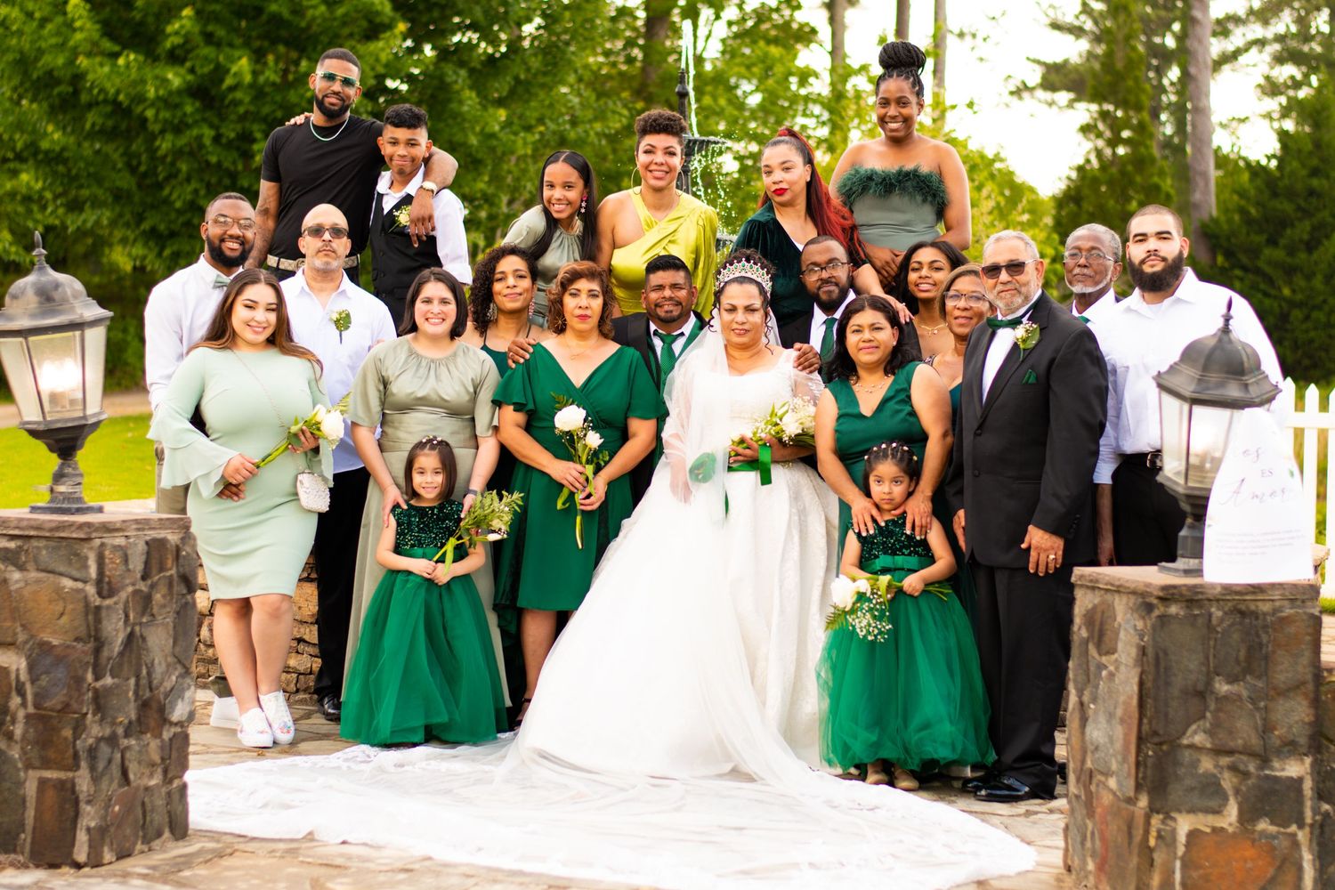Large wedding party posed on stone steps wearing green and white formal attire.