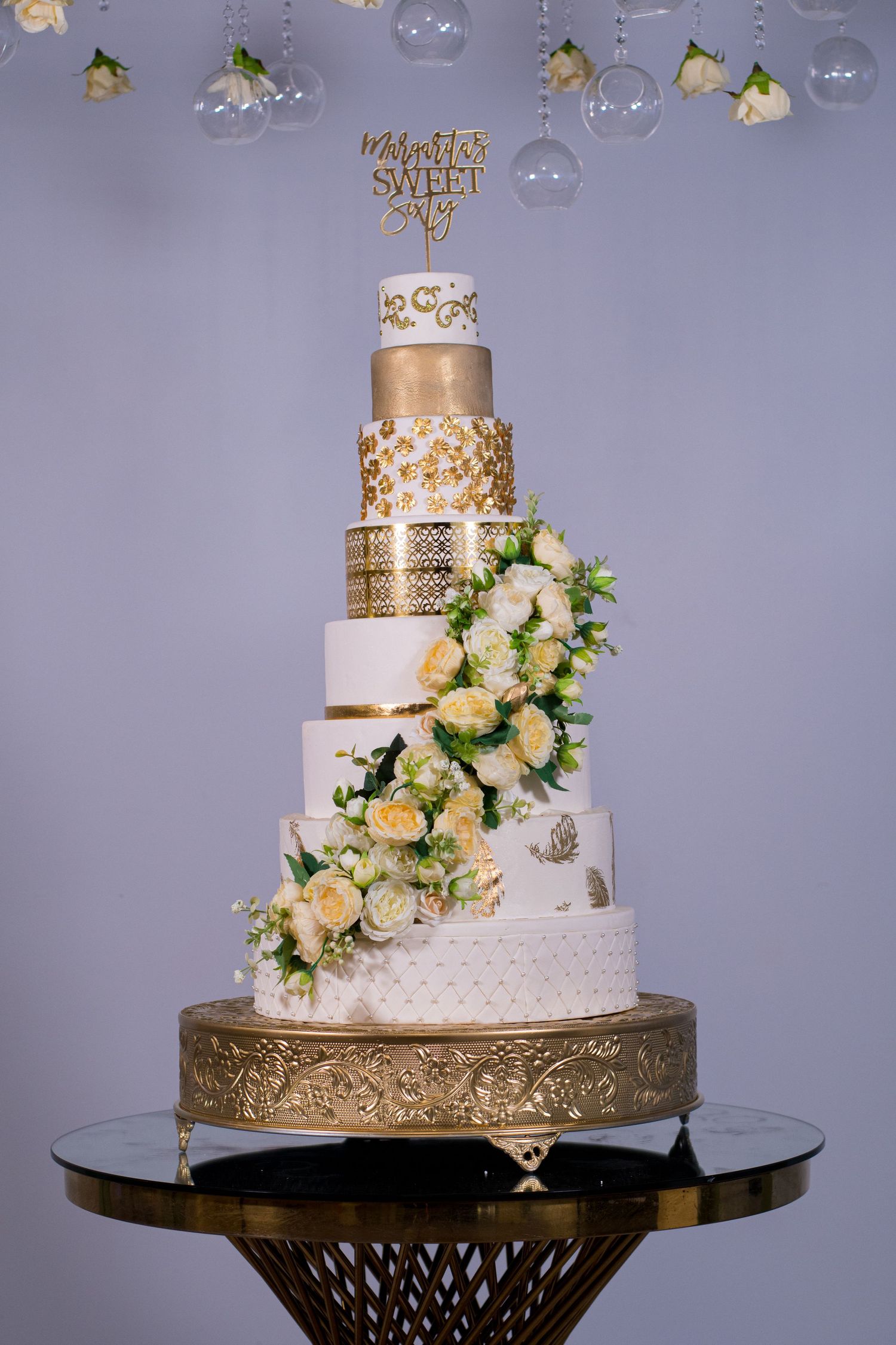 Six-tier white and gold wedding cake adorned with cascading flowers and metallic details.