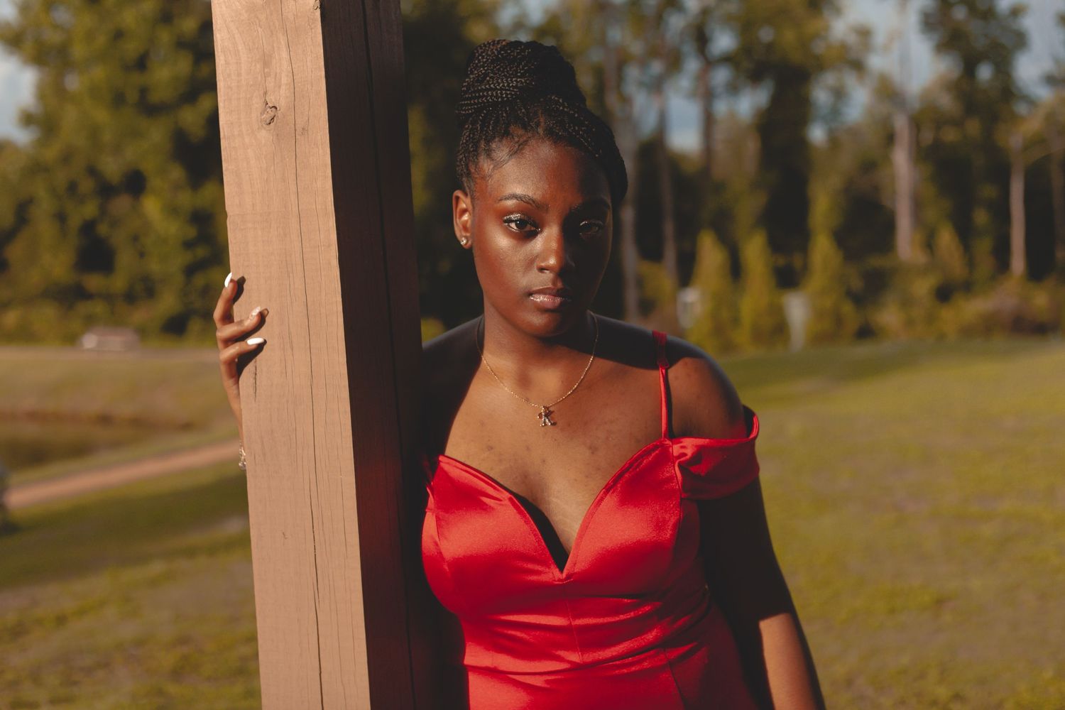 A person in a striking red dress poses dramatically against a wooden post at sunset.