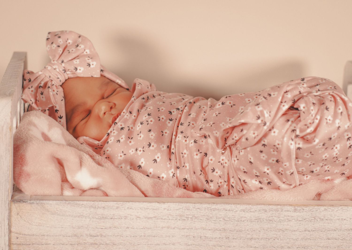 Newborn baby sleeping peacefully in pink floral swaddle blanket.