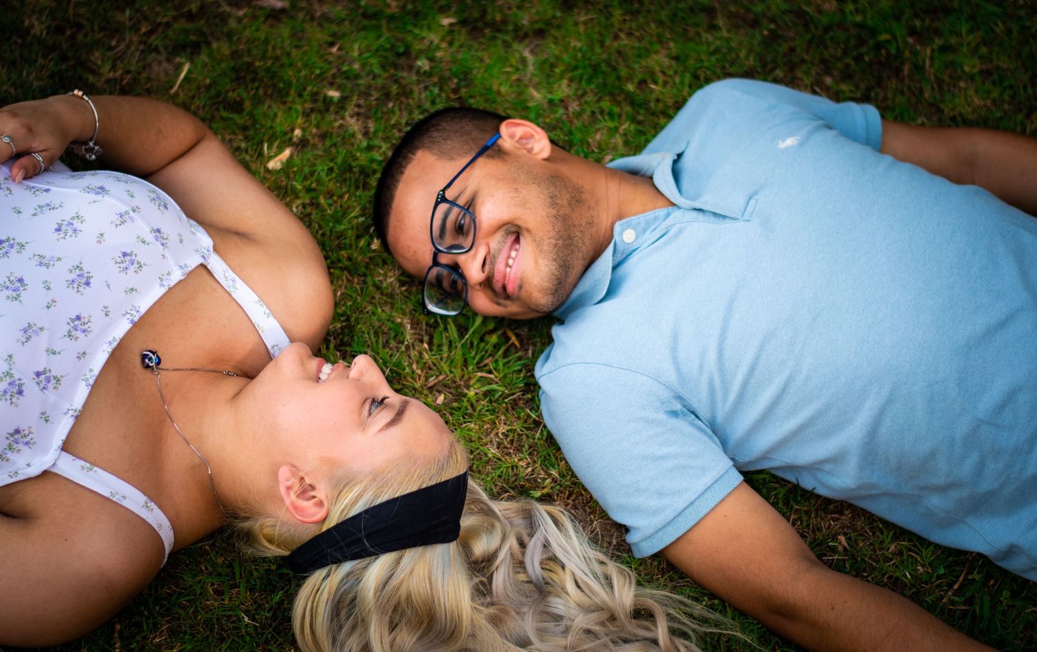 Couple lying in grass sharing a romantic moment outdoors with joyful expressions.