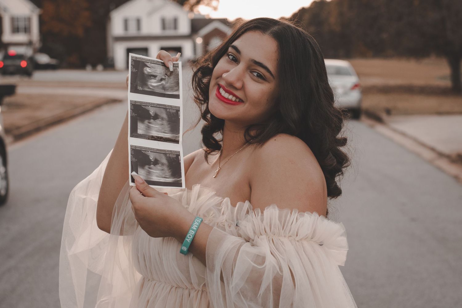 A person in an off-shoulder dress displays ultrasound photos with joy.