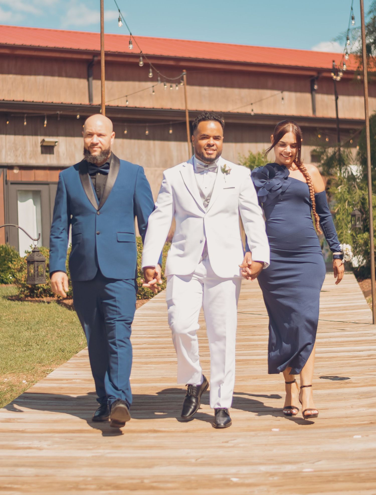 Happy couple in blue and white attire walk together down an outdoor landscaped pathway during celebration.