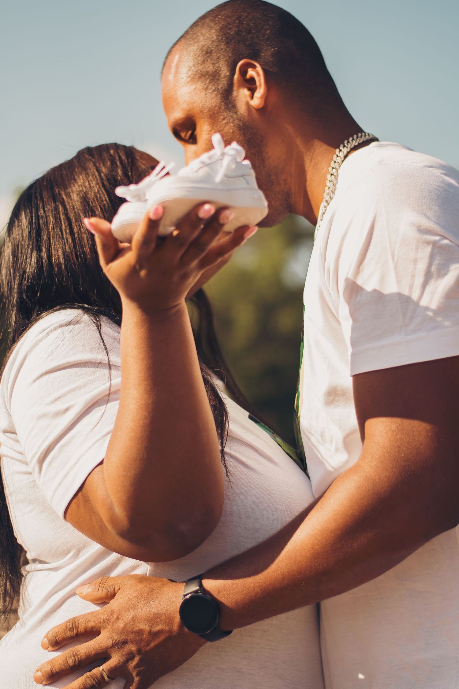 Couple sharing intimate moment with baby shoes during pregnancy photoshoot.