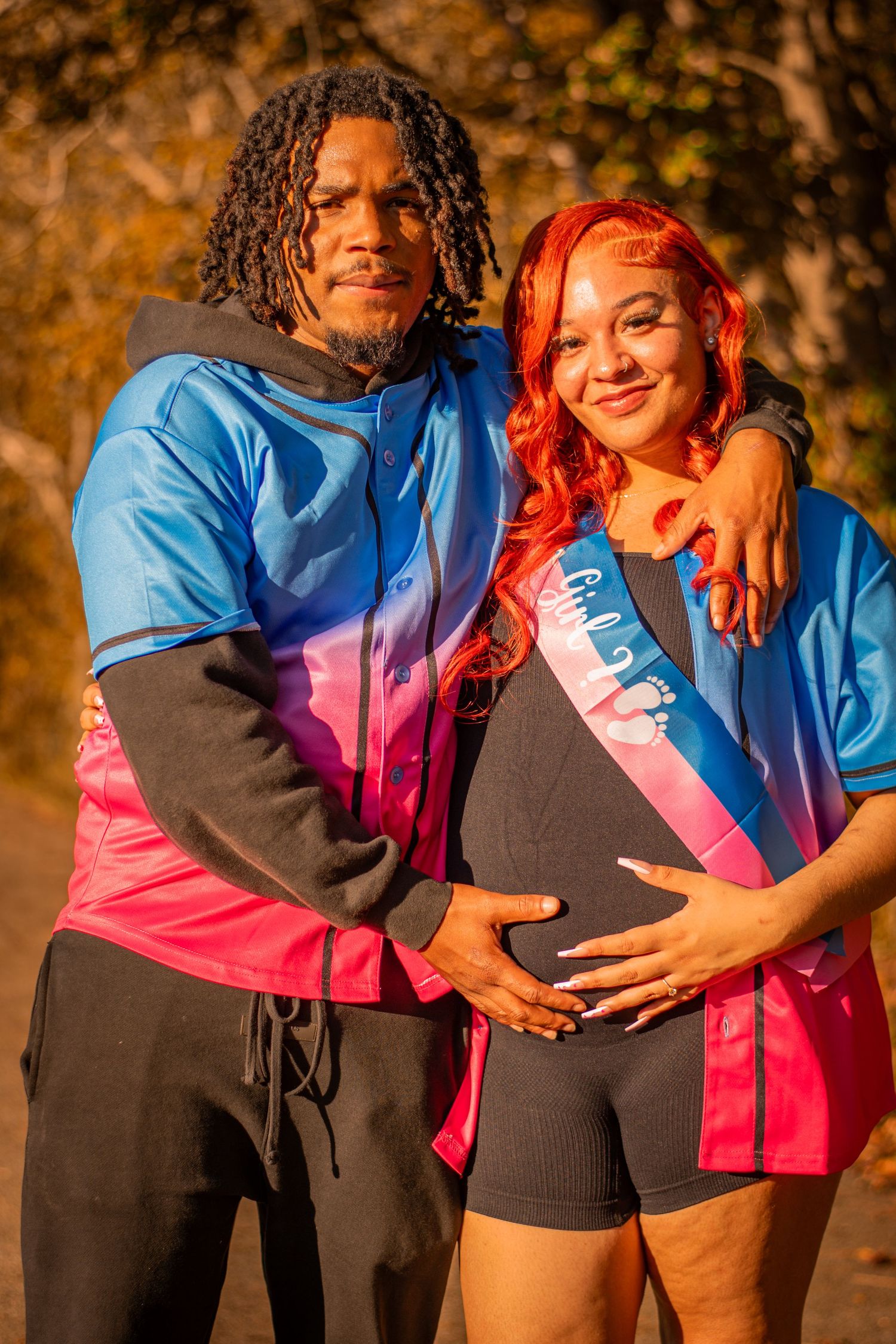 A couple in coordinating blue and pink outfits poses for a pregnancy announcement photo.