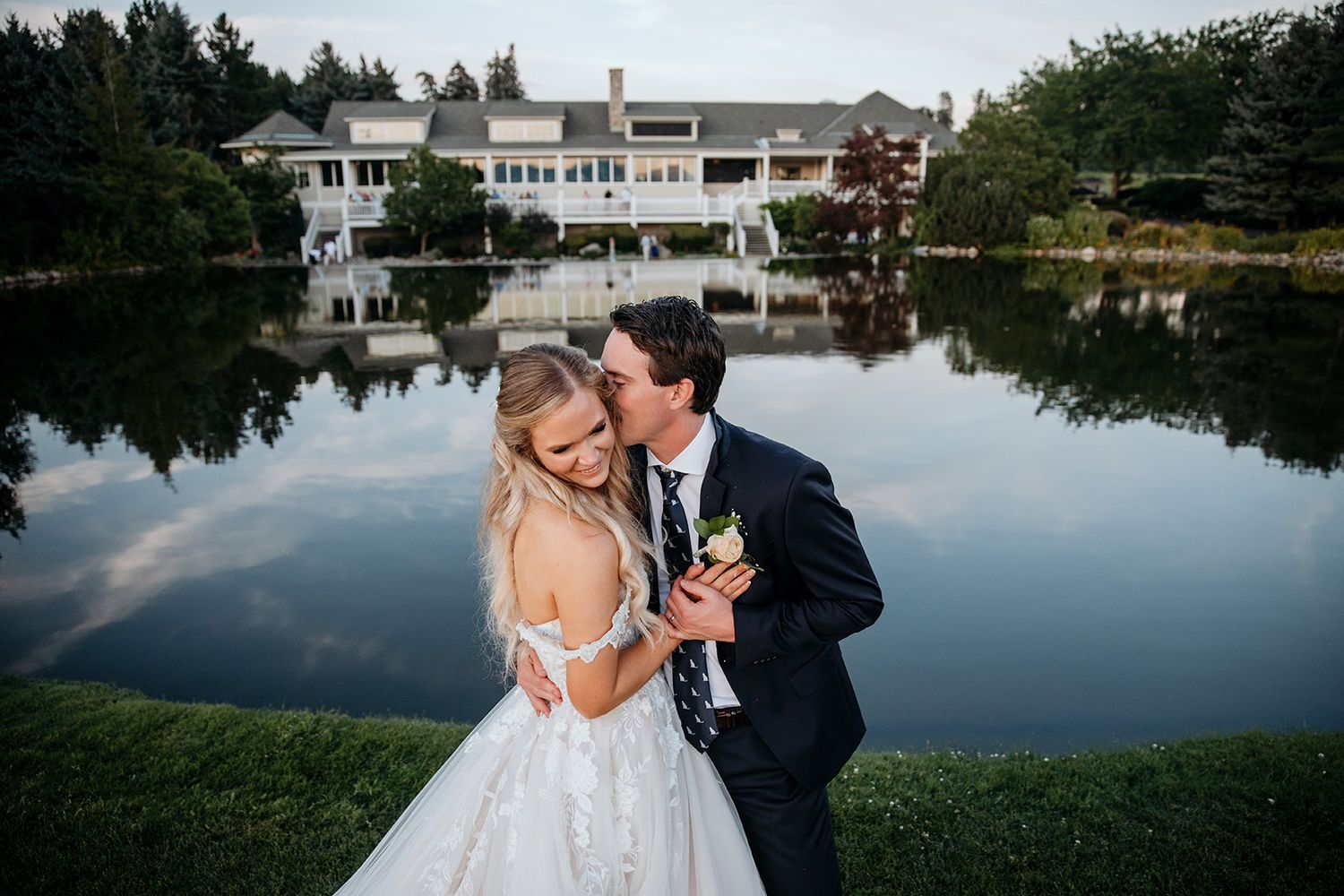 Elegant wedding couple shares romantic moments by a serene lake with reflections at sunset.