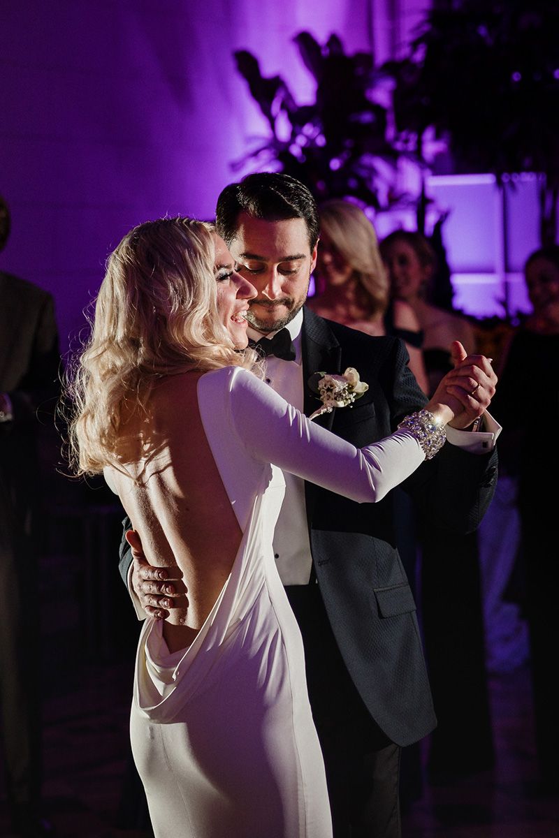 A couple dances together in an intimate moment on a dark dance floor illuminated by purple lighting.