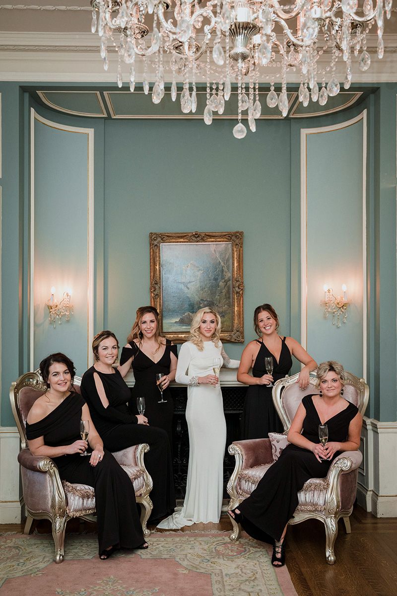 Wedding party poses playfully on vintage furniture in an elegant room with mint walls and crystal chandeliers.