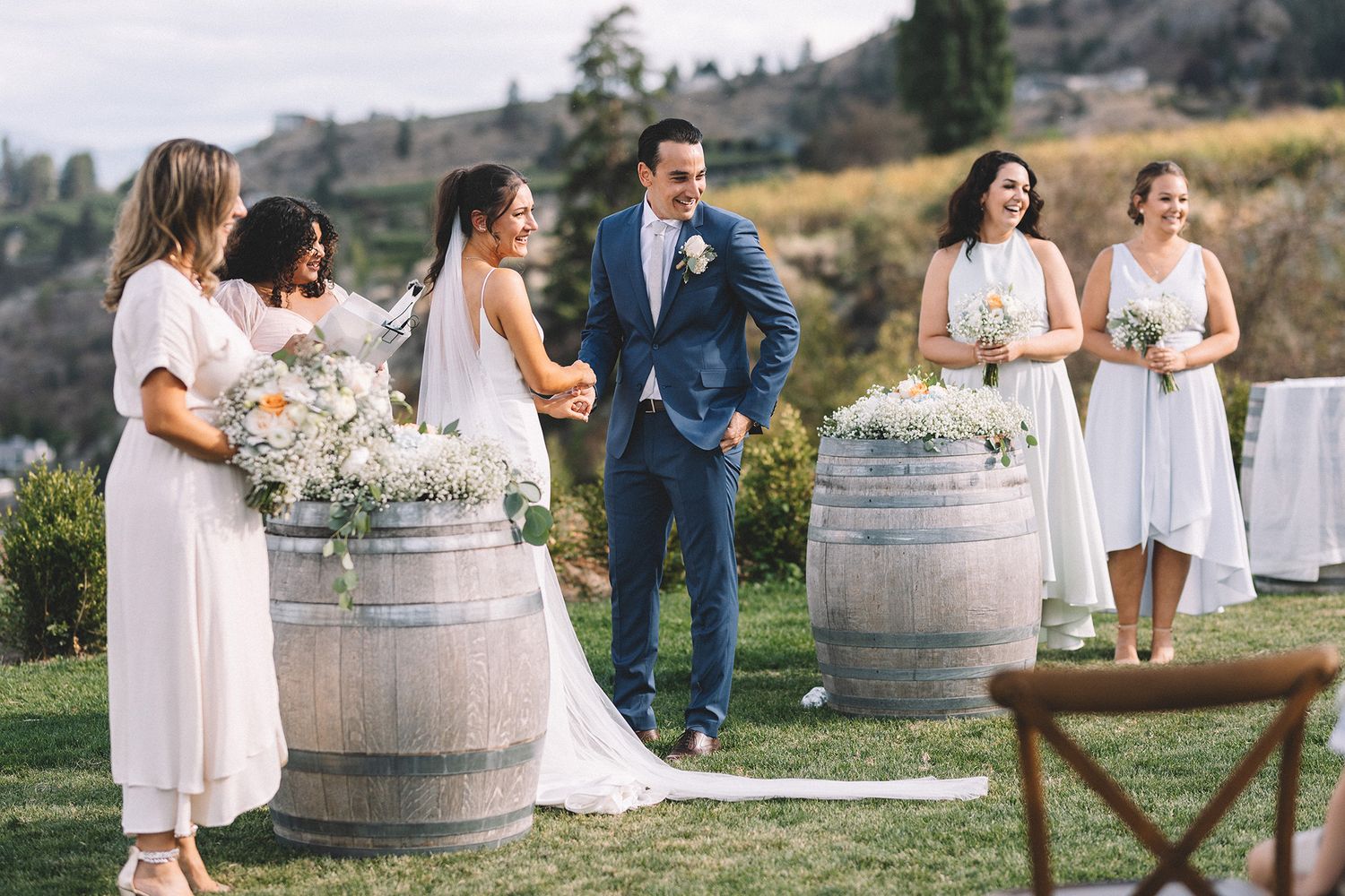 A rustic outdoor wedding celebration with wine barrels and floral arrangements in a scenic mountain setting.