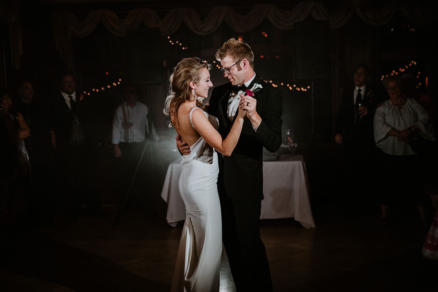 A couple shares their first dance together at a wedding reception with twinkle lights glowing in the background.